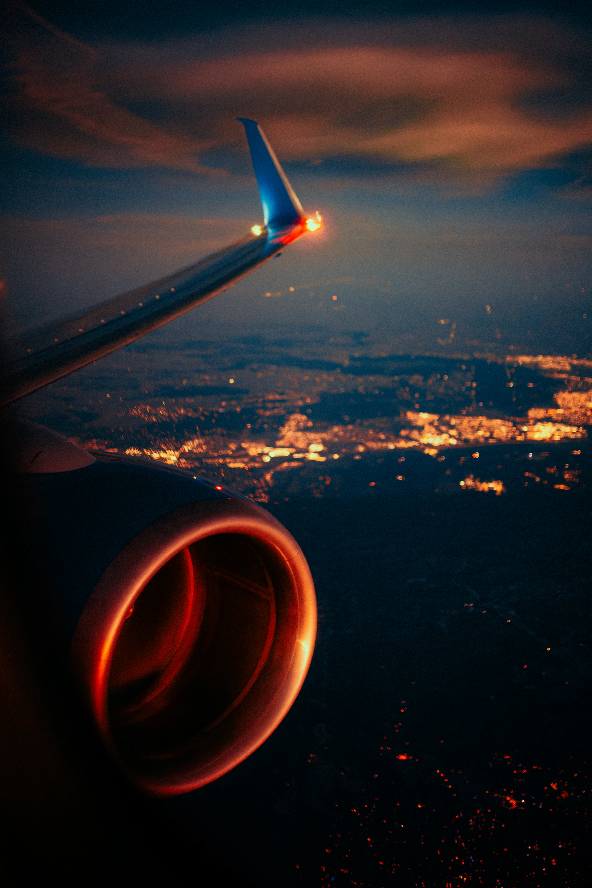 Airplane wing and engine over city lights at night
