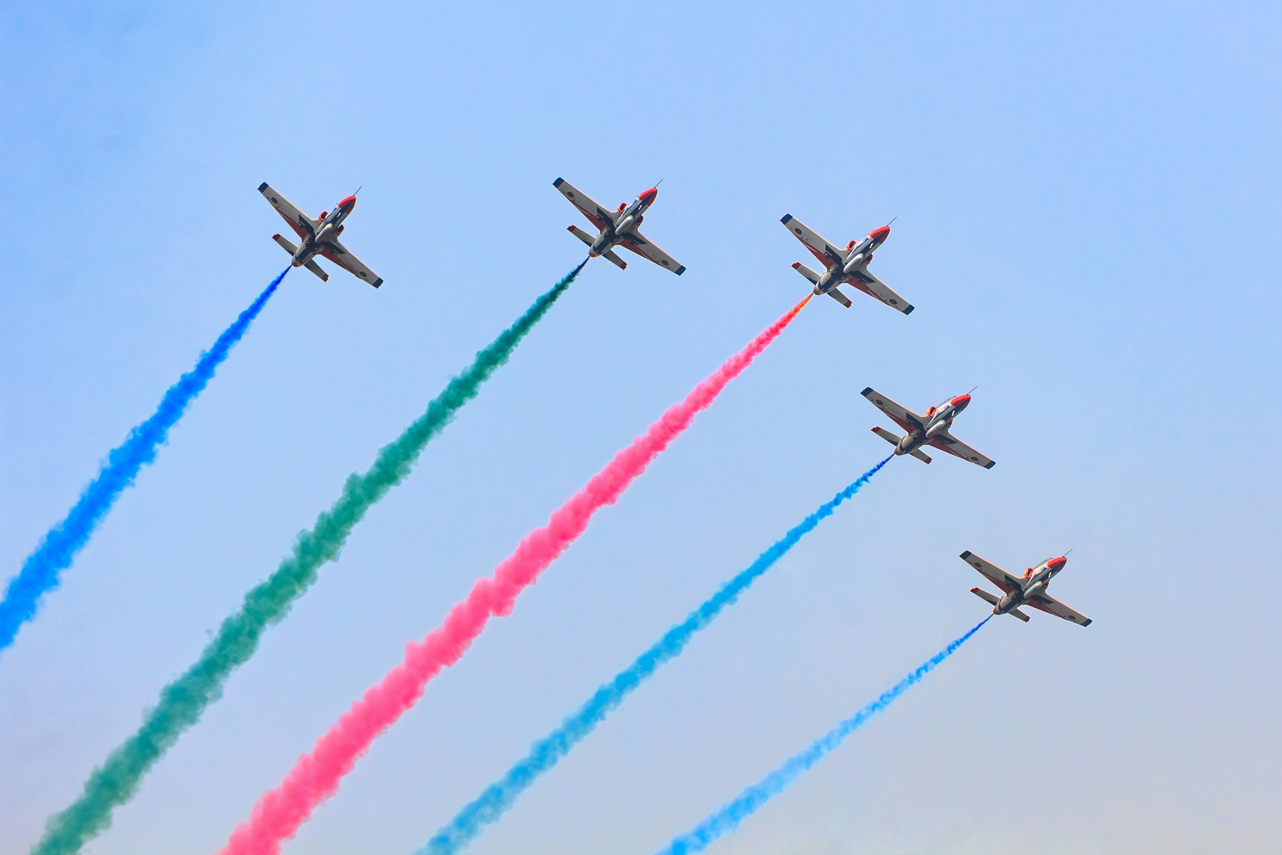 Five planes fly in formation leaving colored smoke trails.