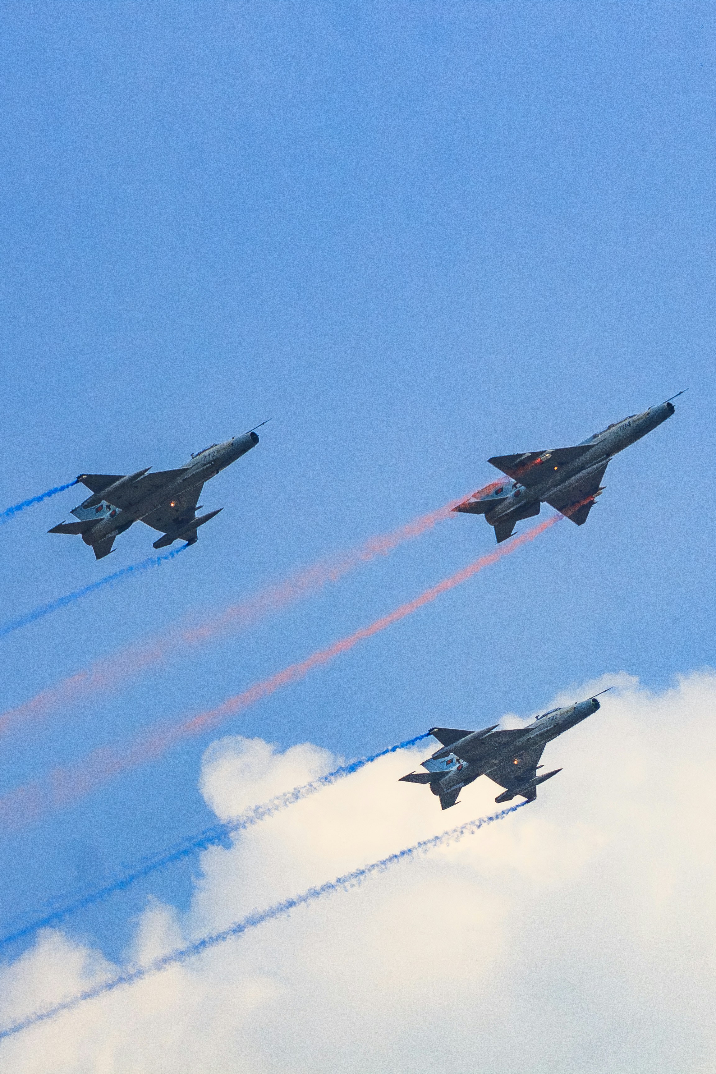 Three fighter jets fly in formation, leaving smoke trails.