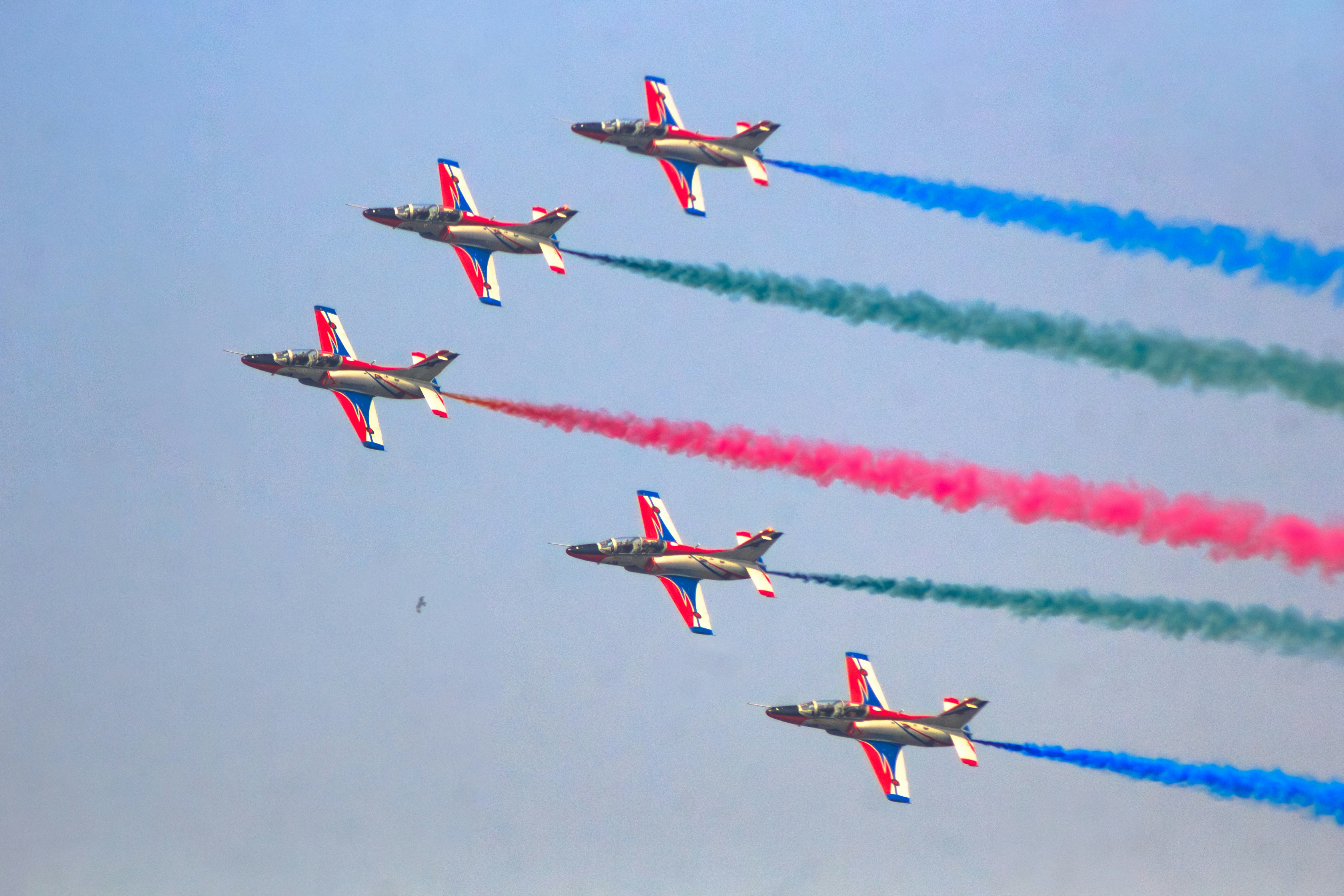 Five jets fly in formation, trailing colored smoke.