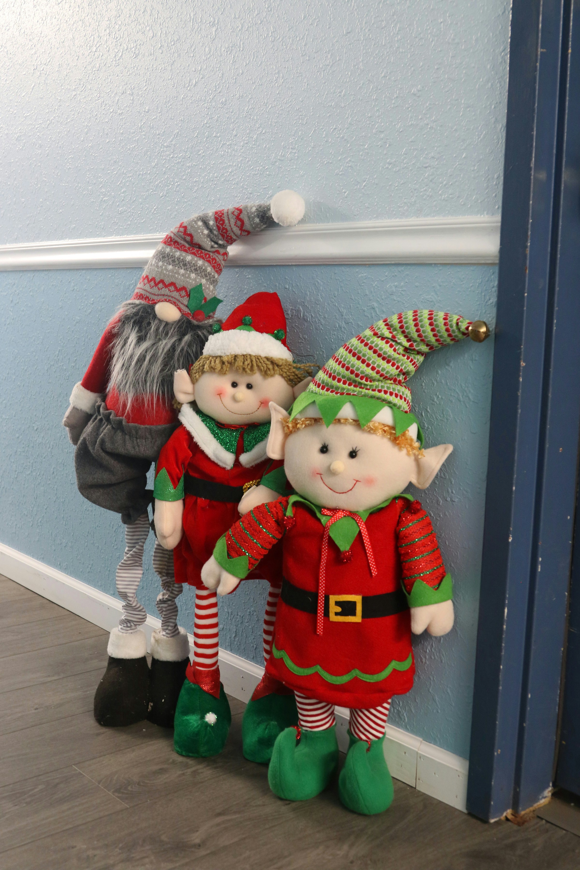 Three christmas elves standing against a wall.