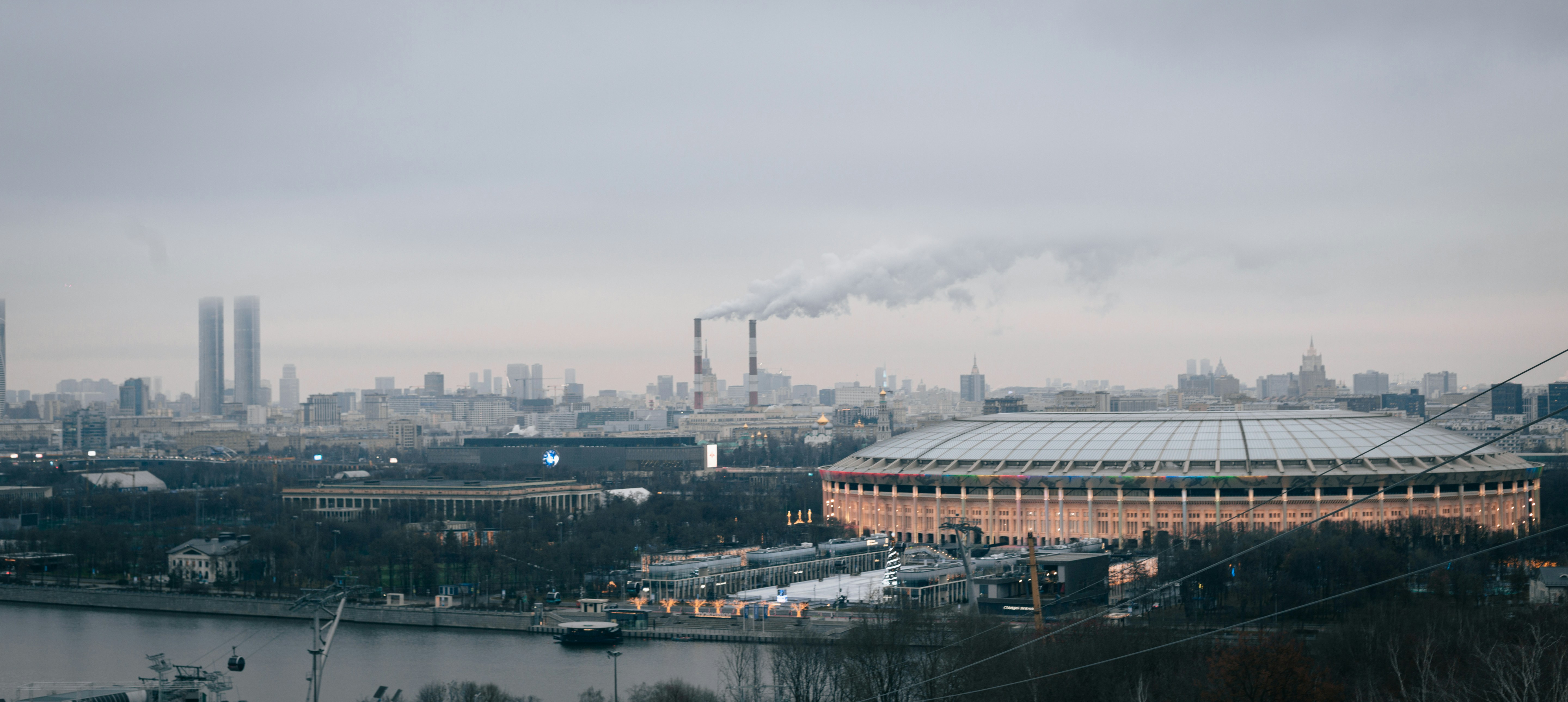Cityscape with stadium and smoking chimneys under cloudy sky