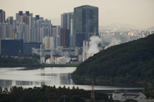 Industrial complex with steam rising near city buildings.