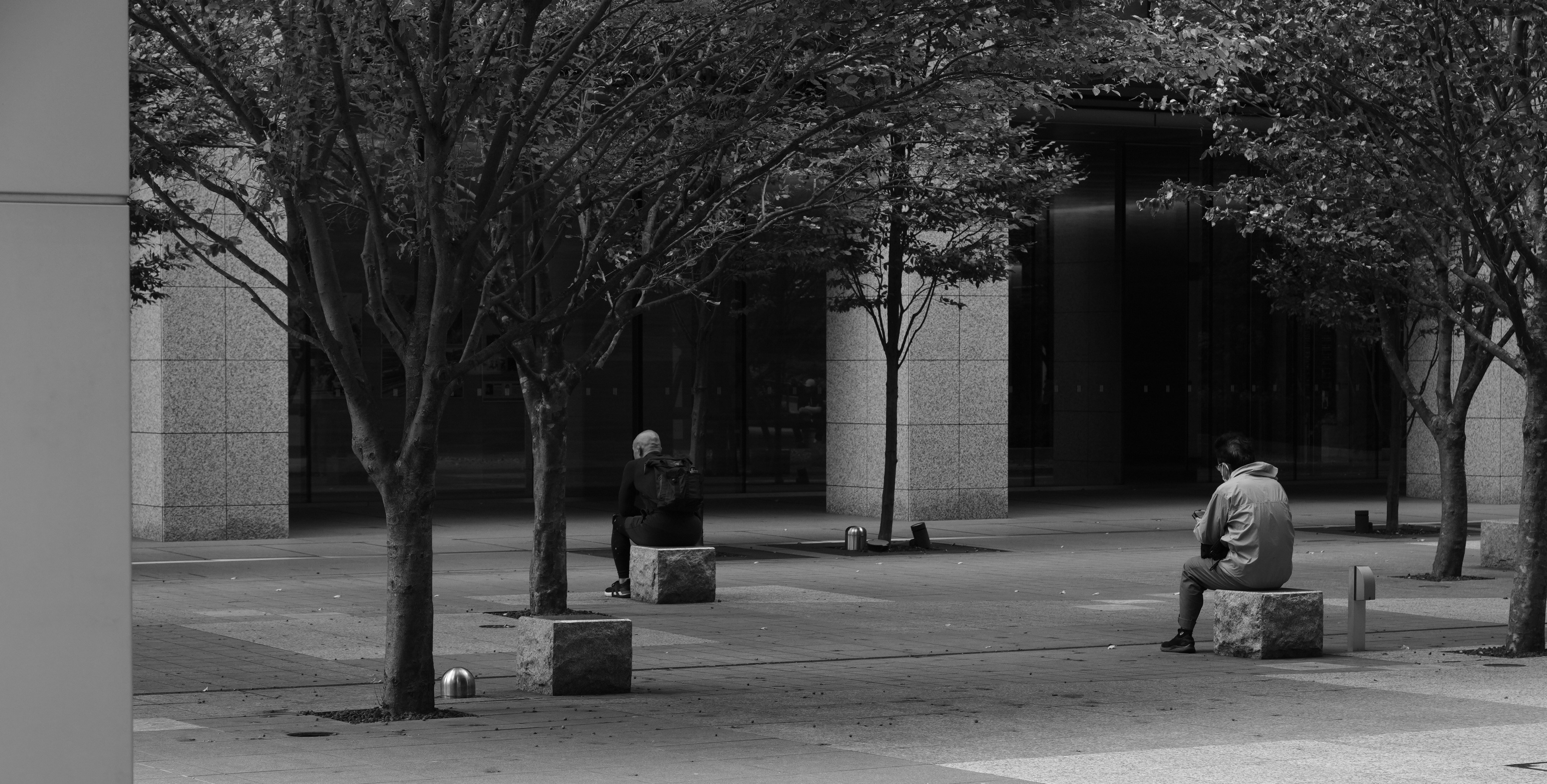 Two people sit on stone benches in a park.