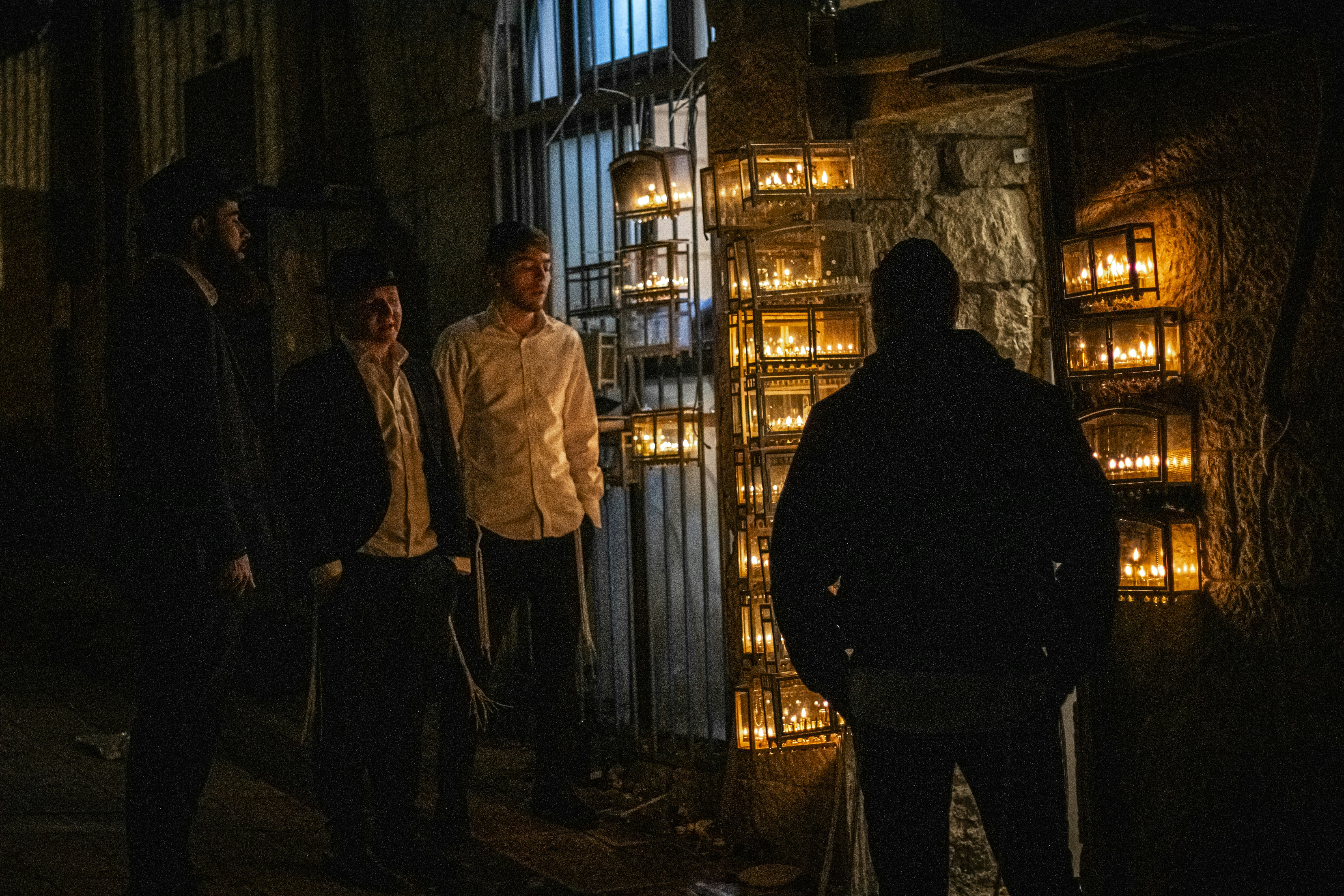 Men stand near wall of lit lanterns at night.