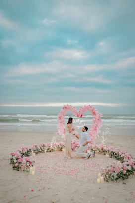Man proposes to woman on beach with heart arch.