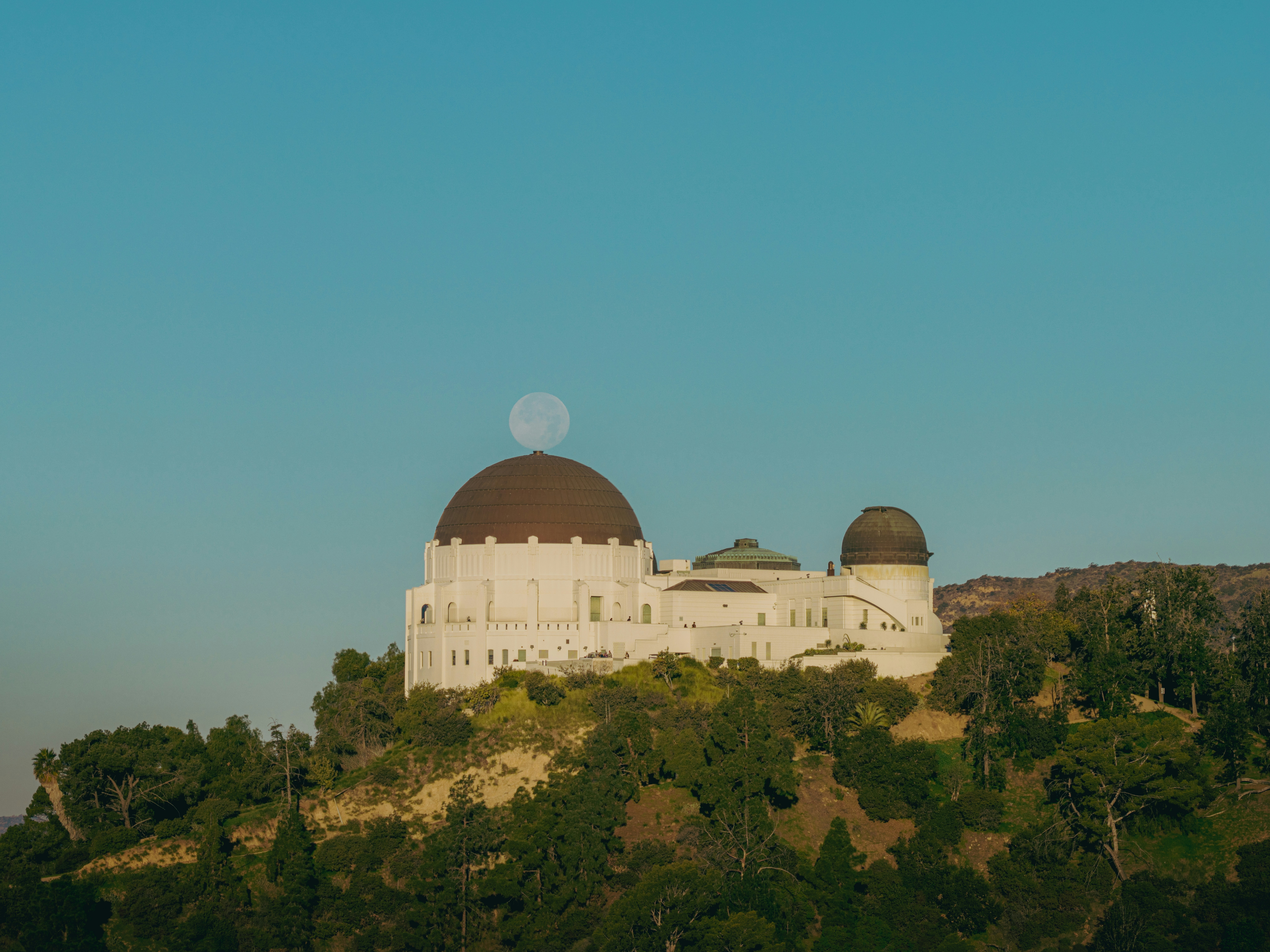 Griffith observatory building with moon behind dome.