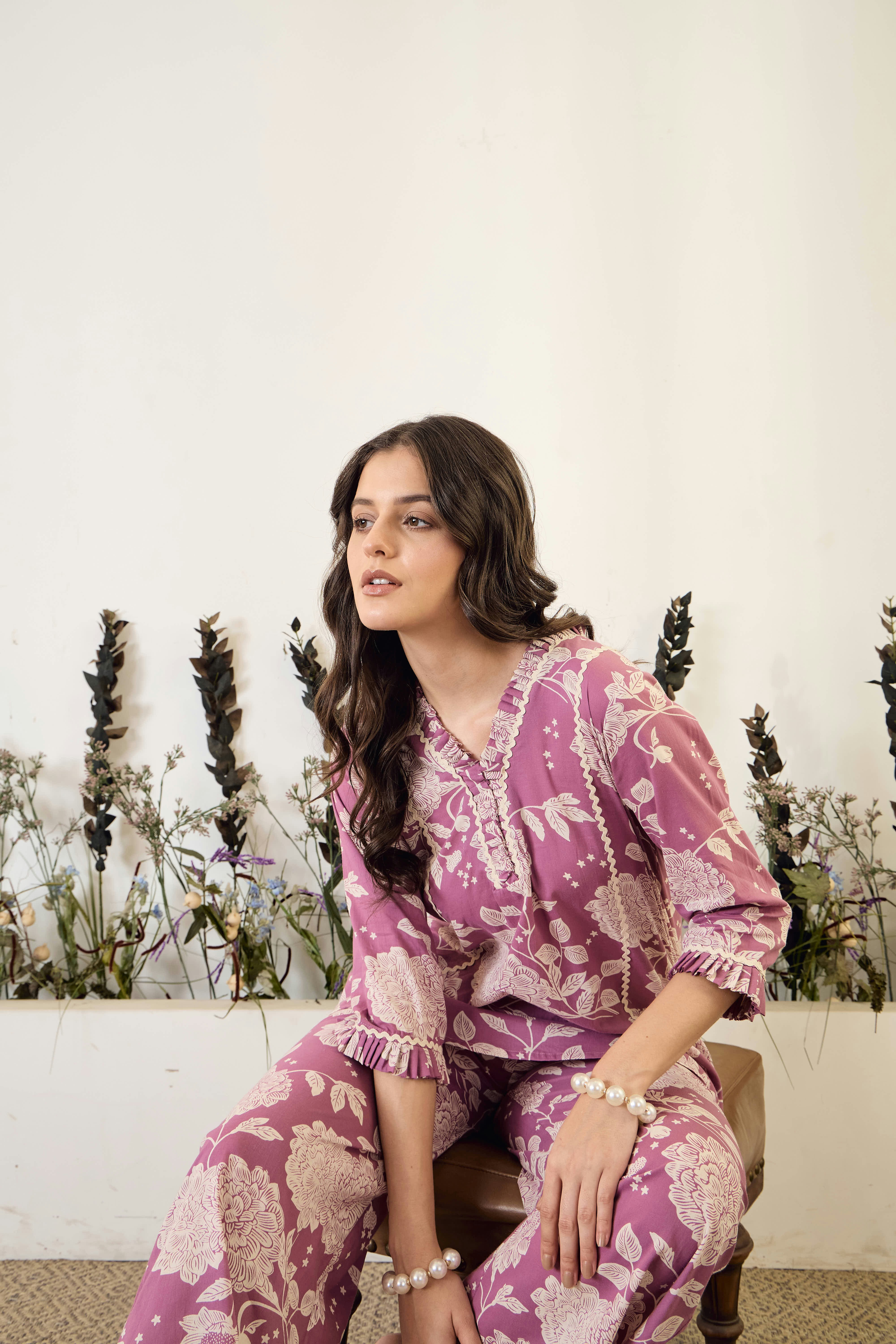 Woman in floral pajamas sits against white wall