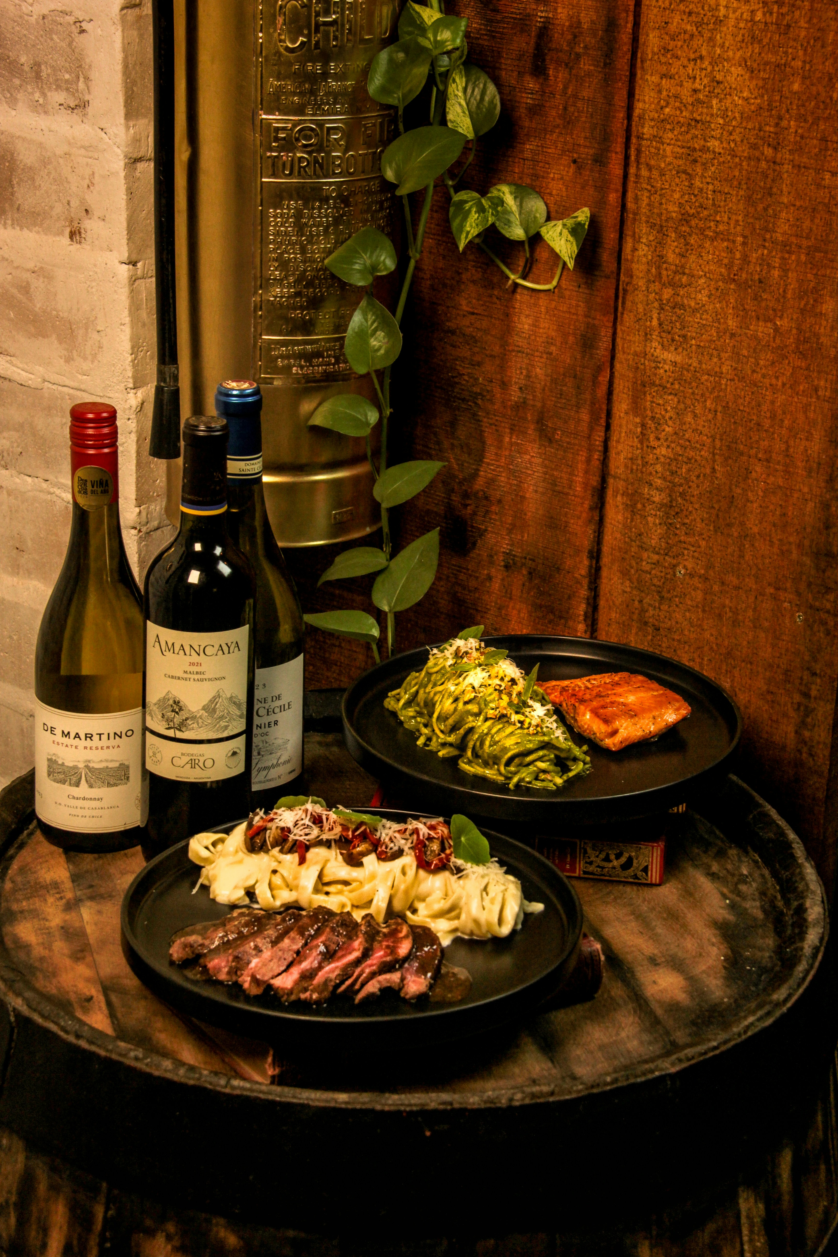 Steak, pasta, and salmon with wine bottles on barrel.