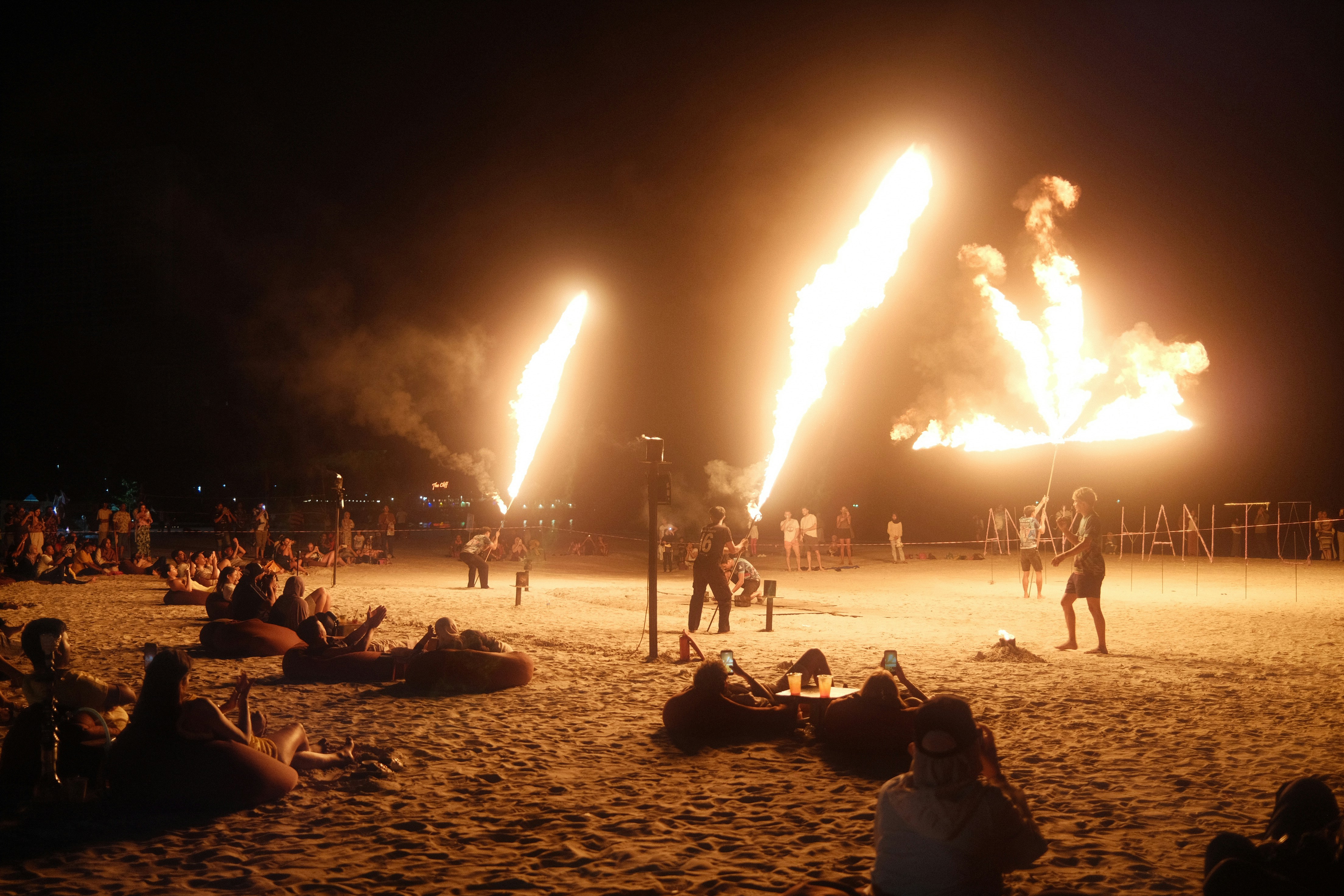 People watch fire performers on a beach at night
