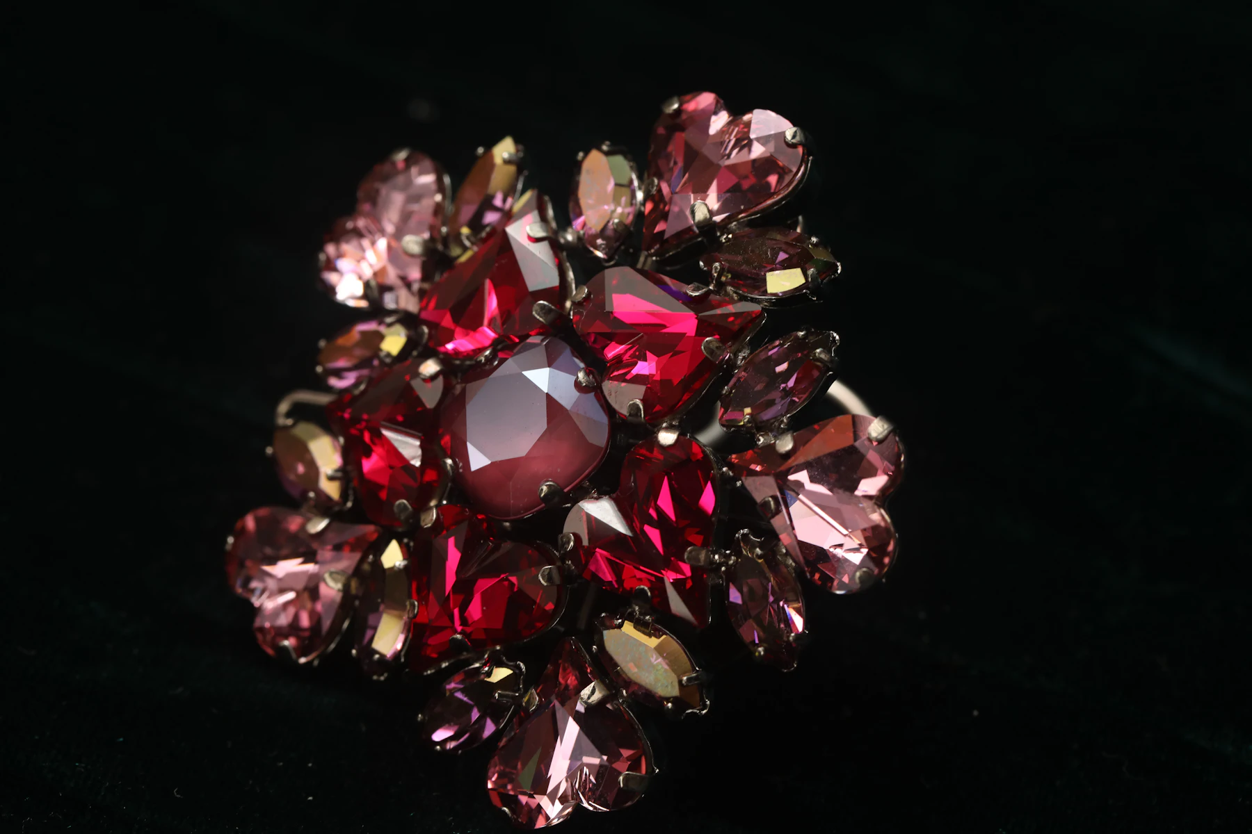 Close-up of a cluster brooch of red and pink rhinestones on a black background, each stone held in a metal prong setting