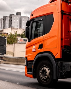 An orange truck drives down a highway.