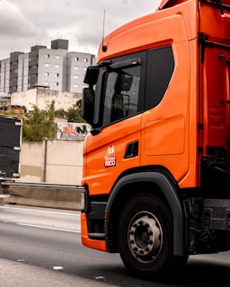 An orange truck drives down a highway.