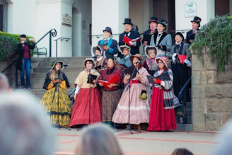 Group of carolers in vintage clothing singing on steps.