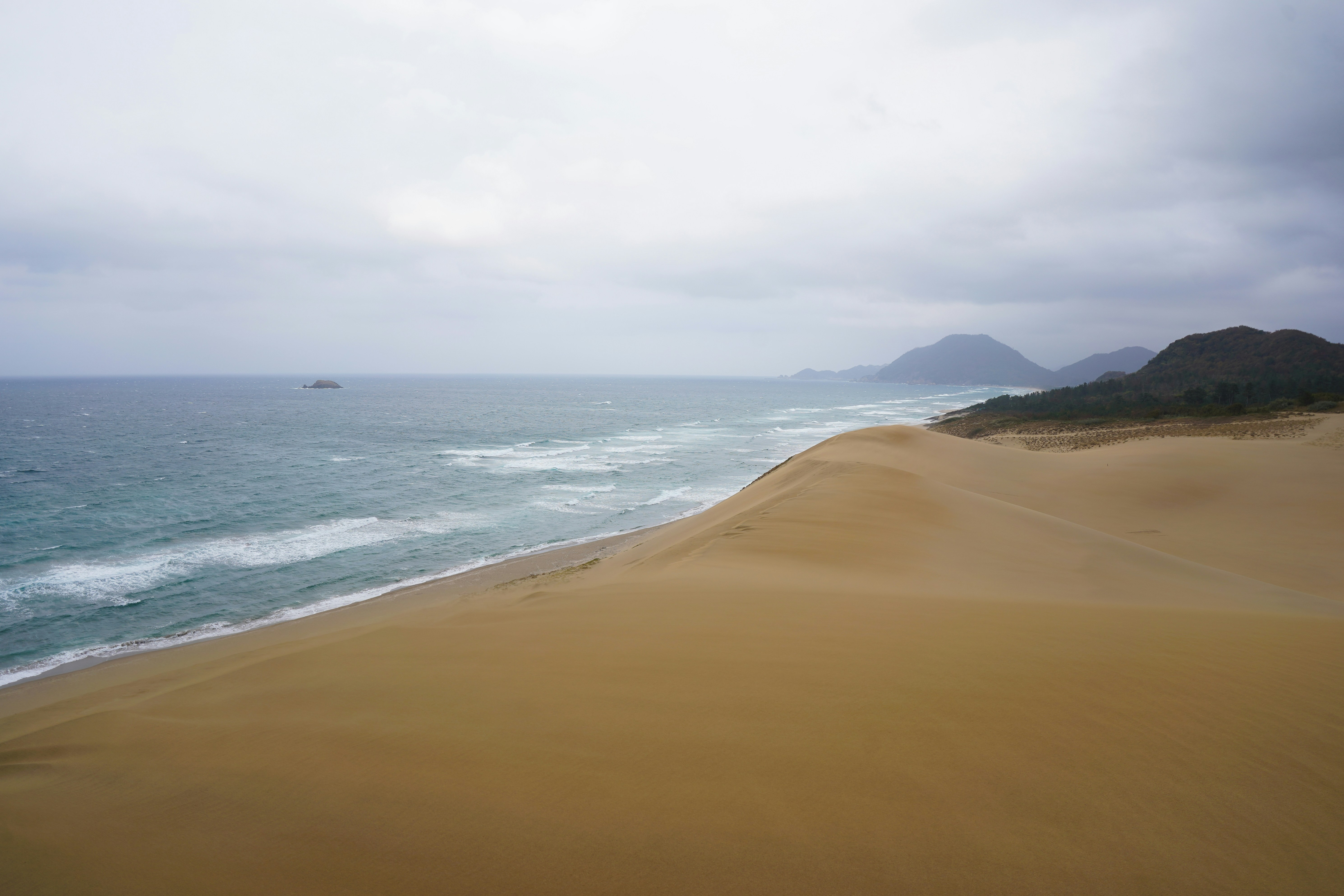 Sandy dunes meet the ocean under a cloudy sky.
