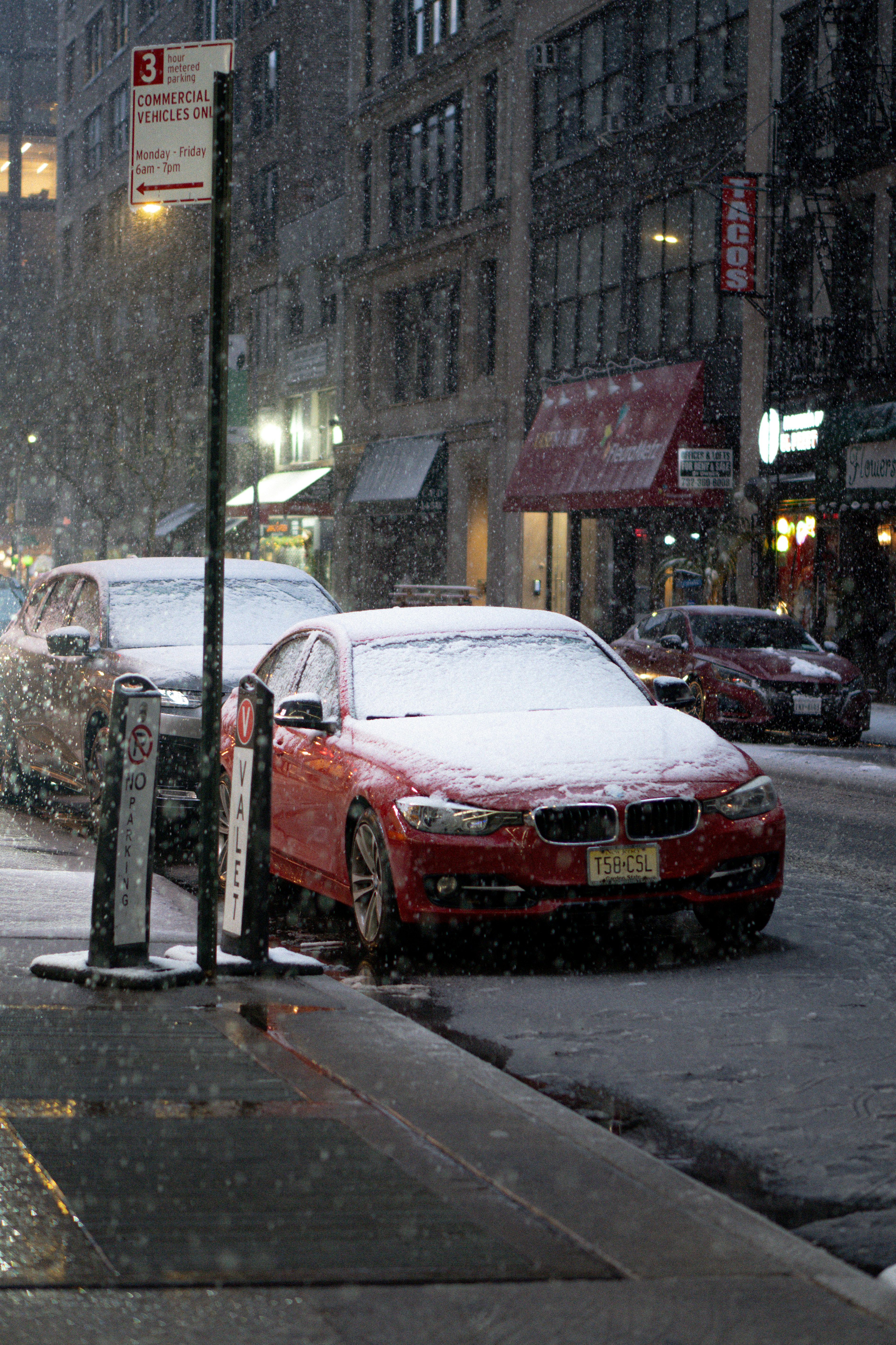 Red car parked on snowy city street at night.