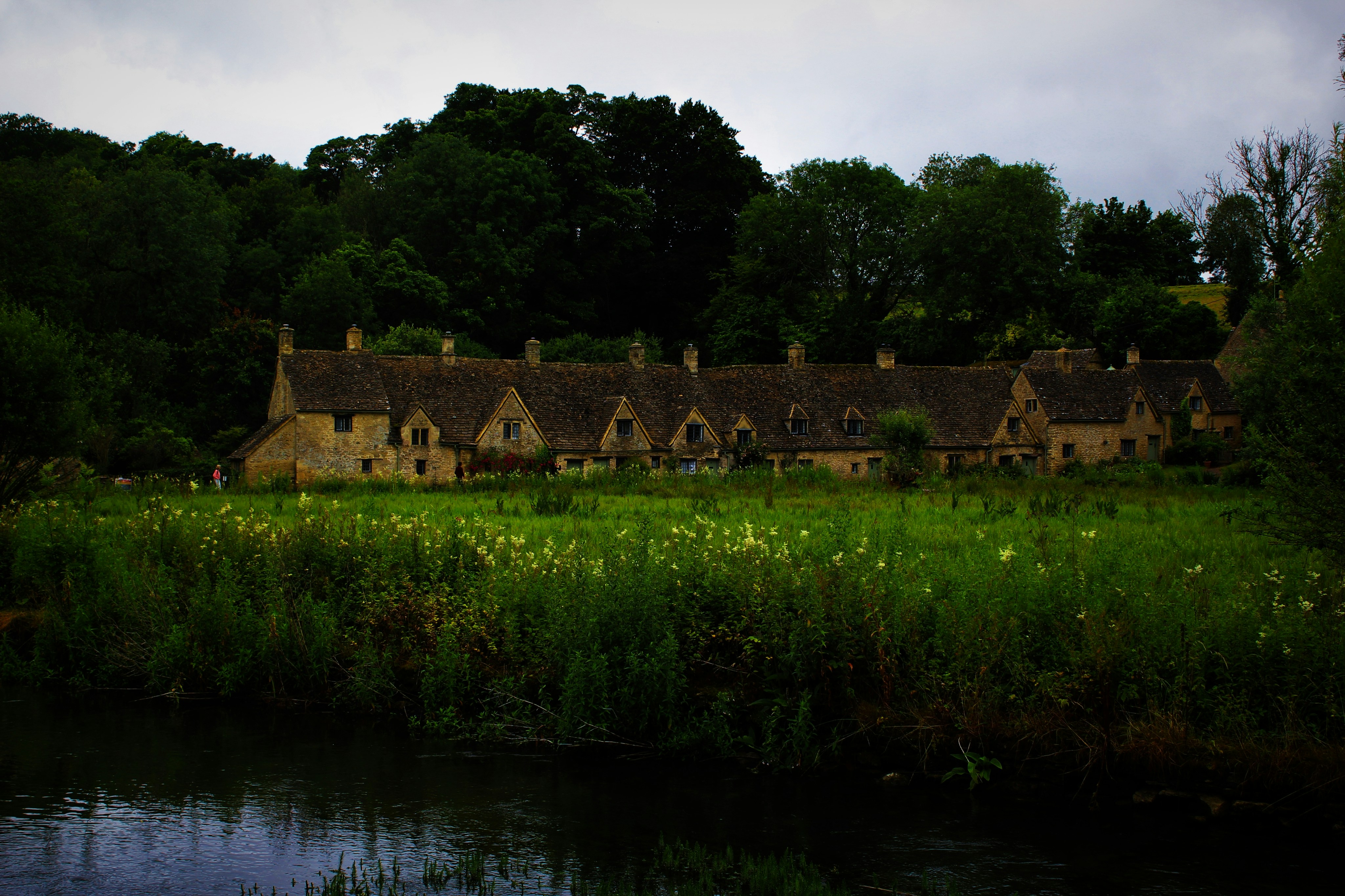 Row of stone cottages beside a grassy field. - Bibury