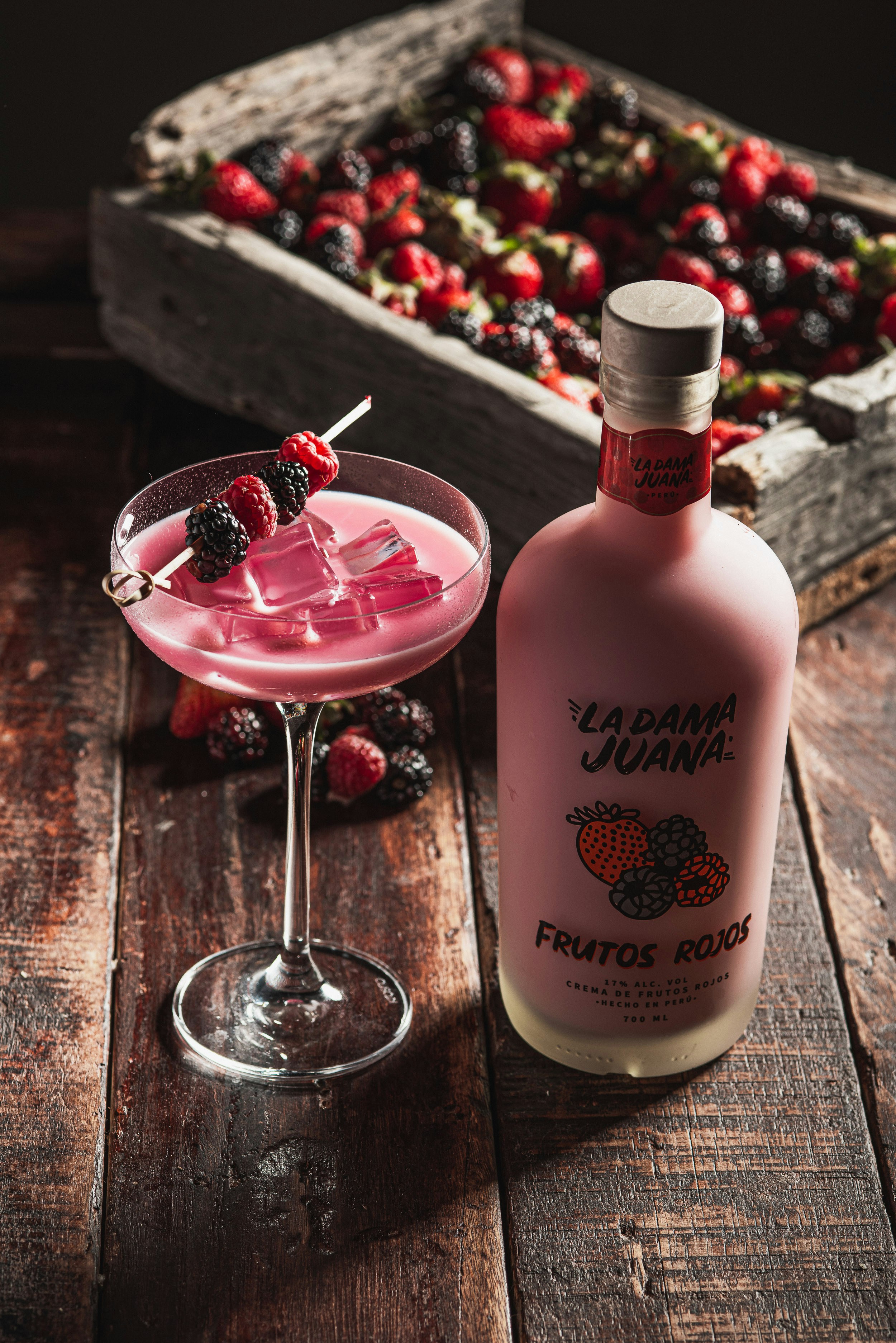 Cocktail di frutti rossi rosa con frutti di bosco freschi e bottiglia di liquore.