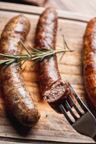 Three browned sausages on a wooden board with rosemary.