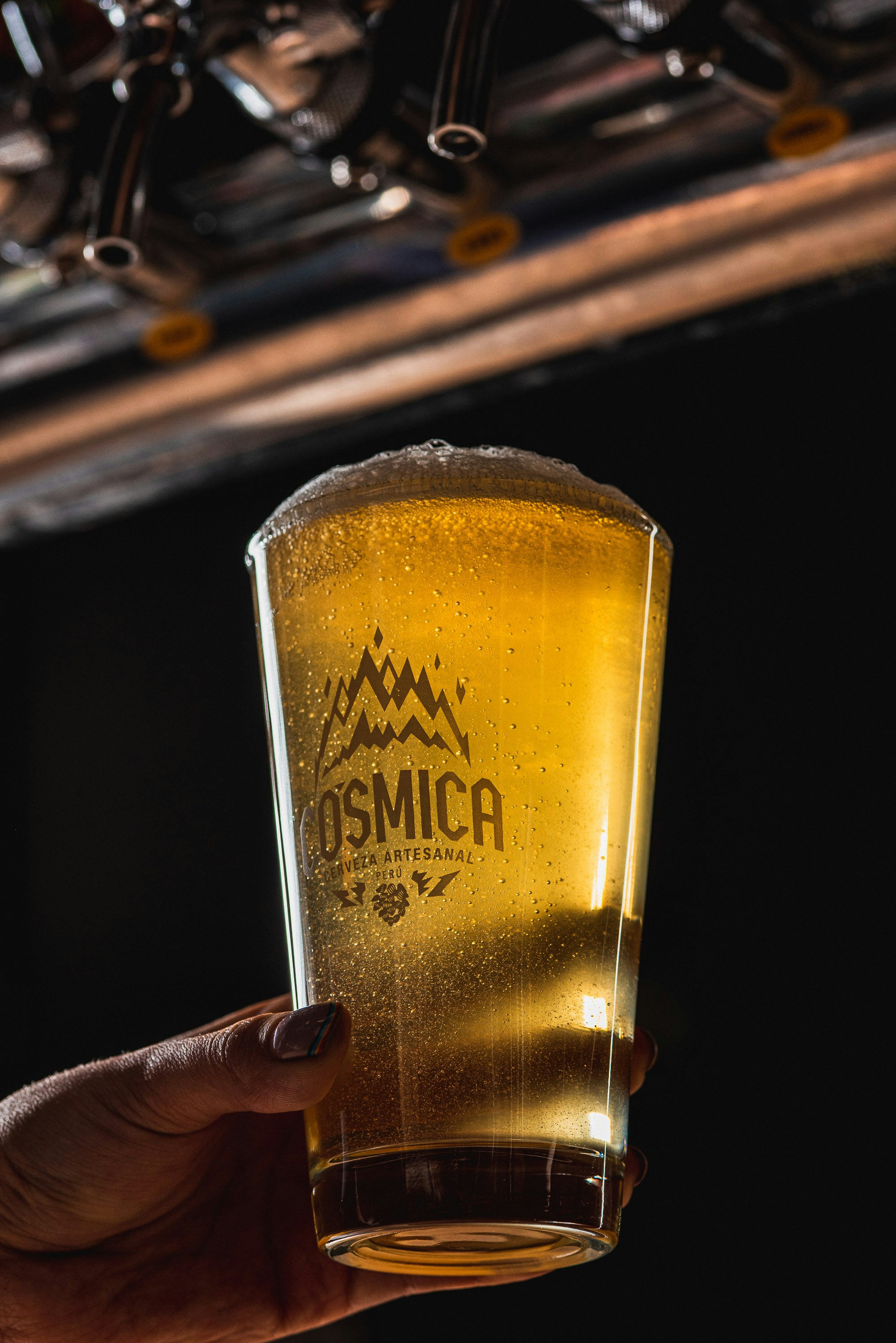 A hand holds a pint of beer with foam head.
