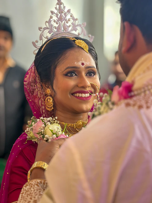 A smiling bride in traditional attire looks at her groom.