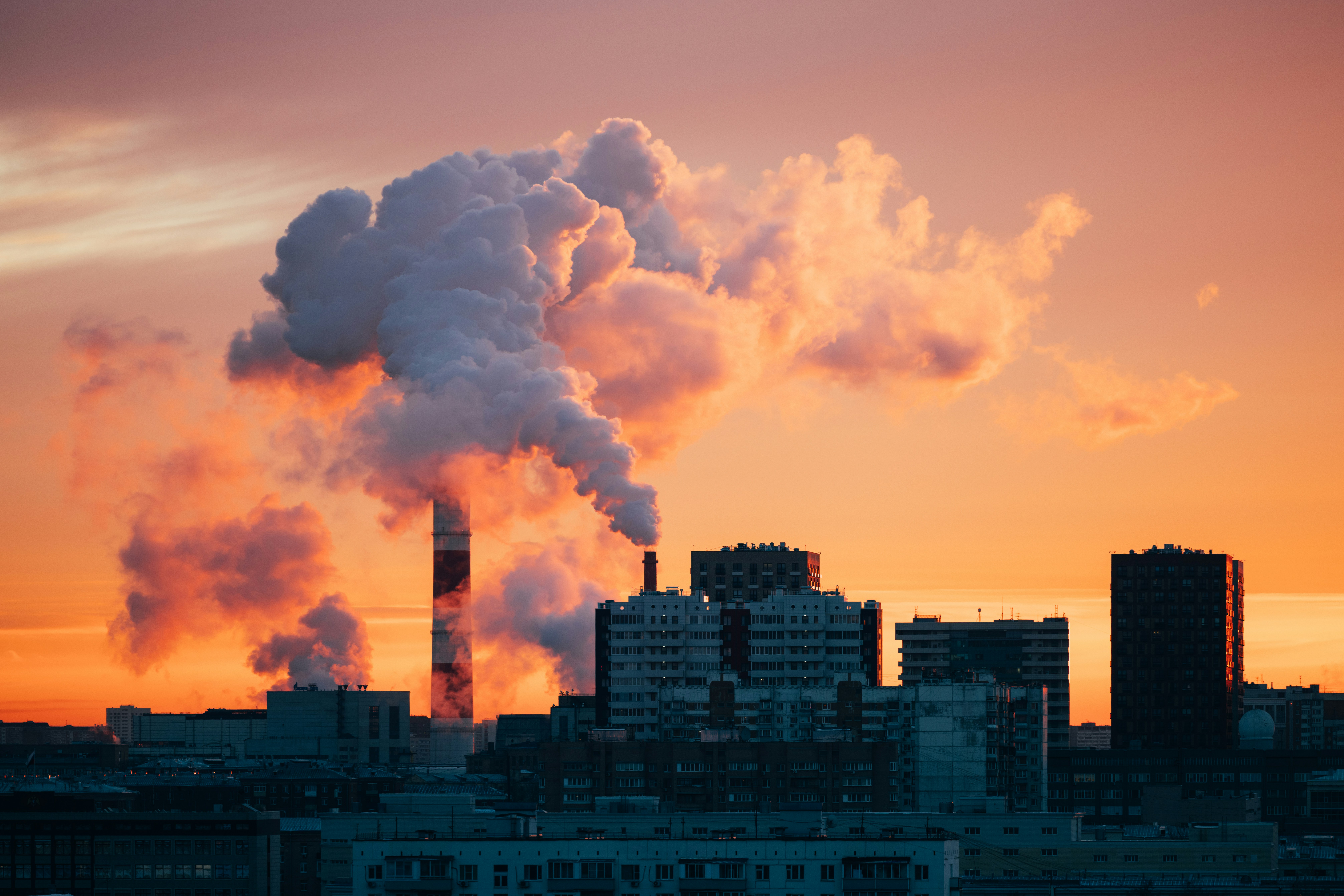 Factory smokestacks emitting smoke against sunset sky