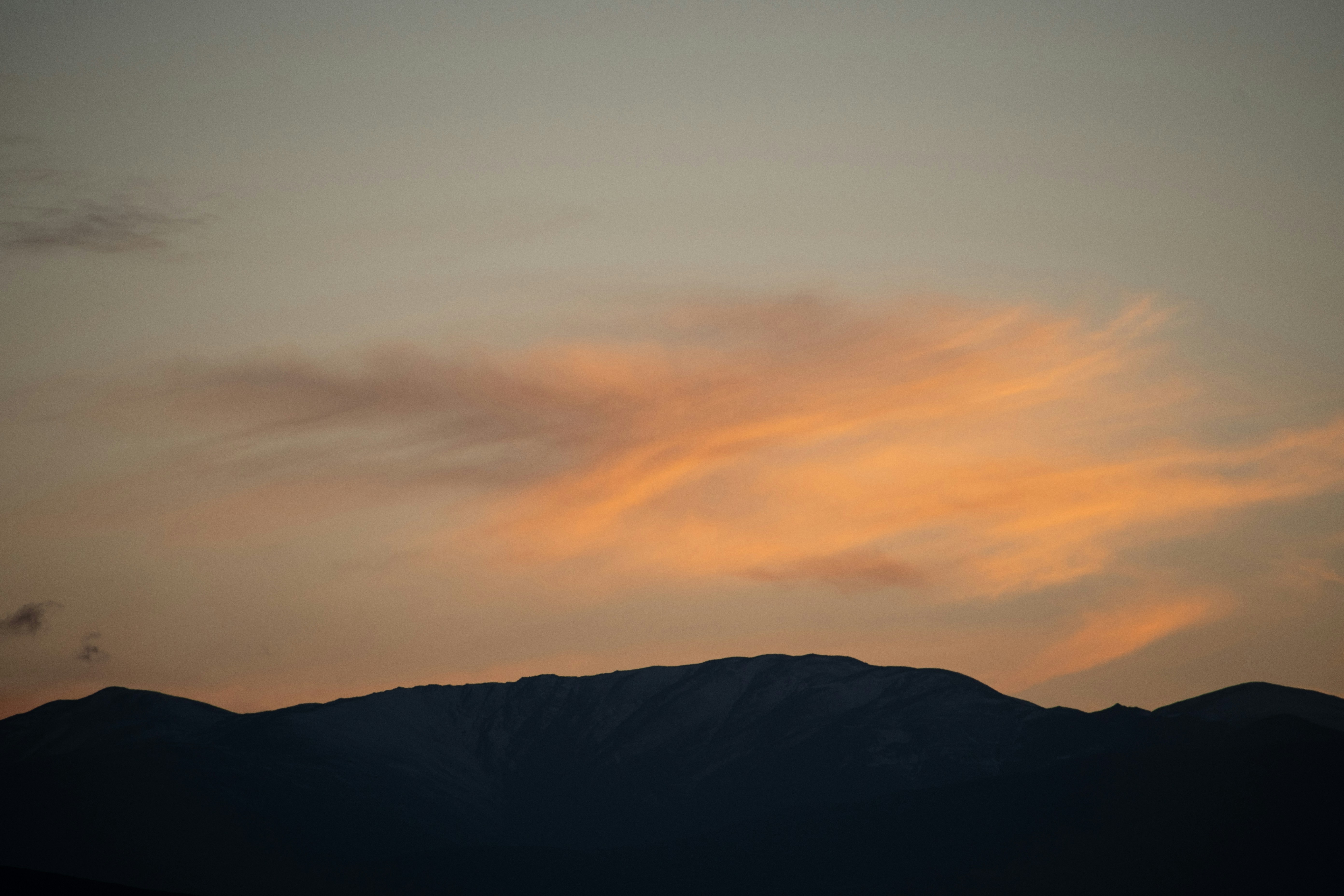 Mountains silhouetted against a soft orange sunset sky