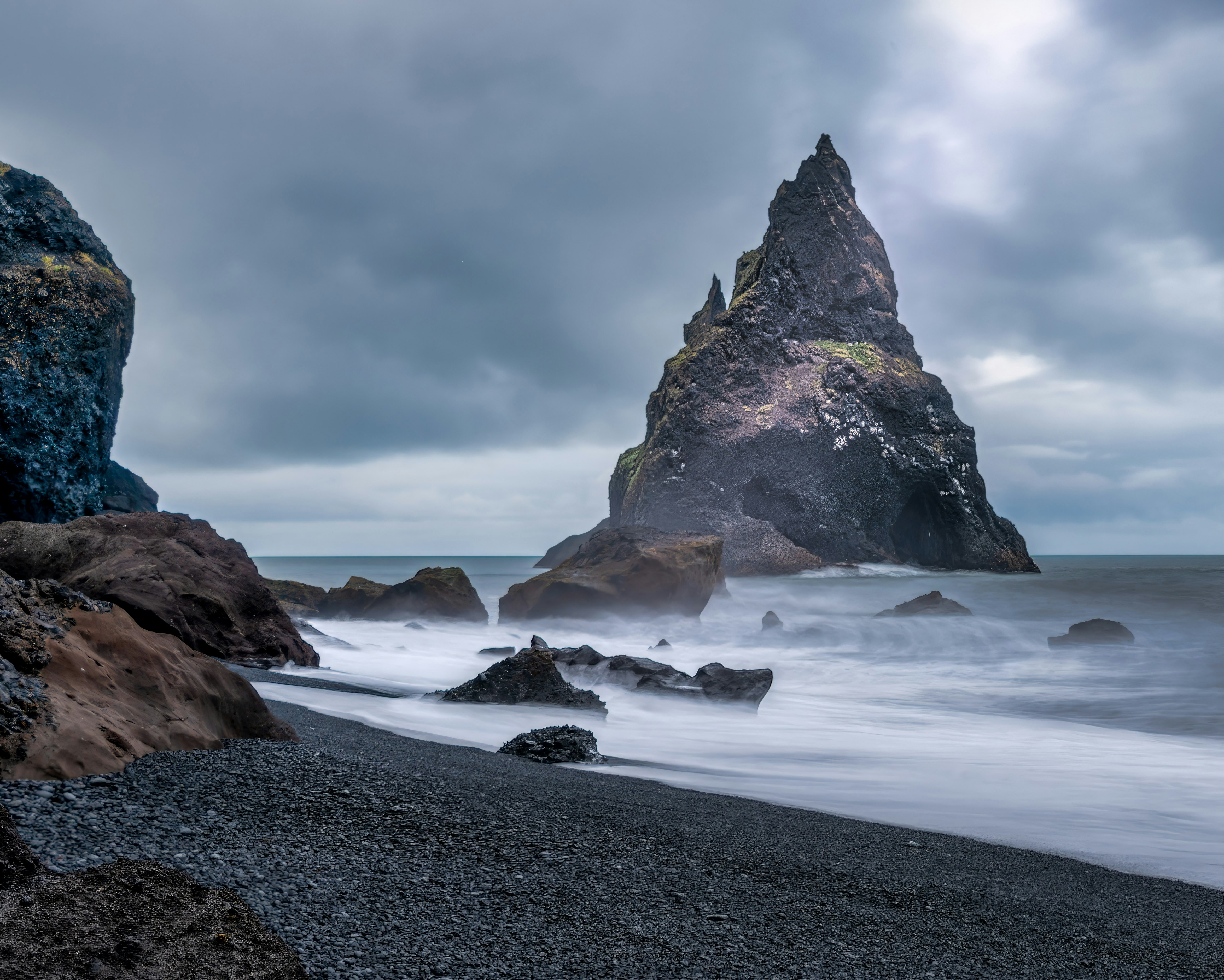 Jagged rock formation on a stormy black sand beach.