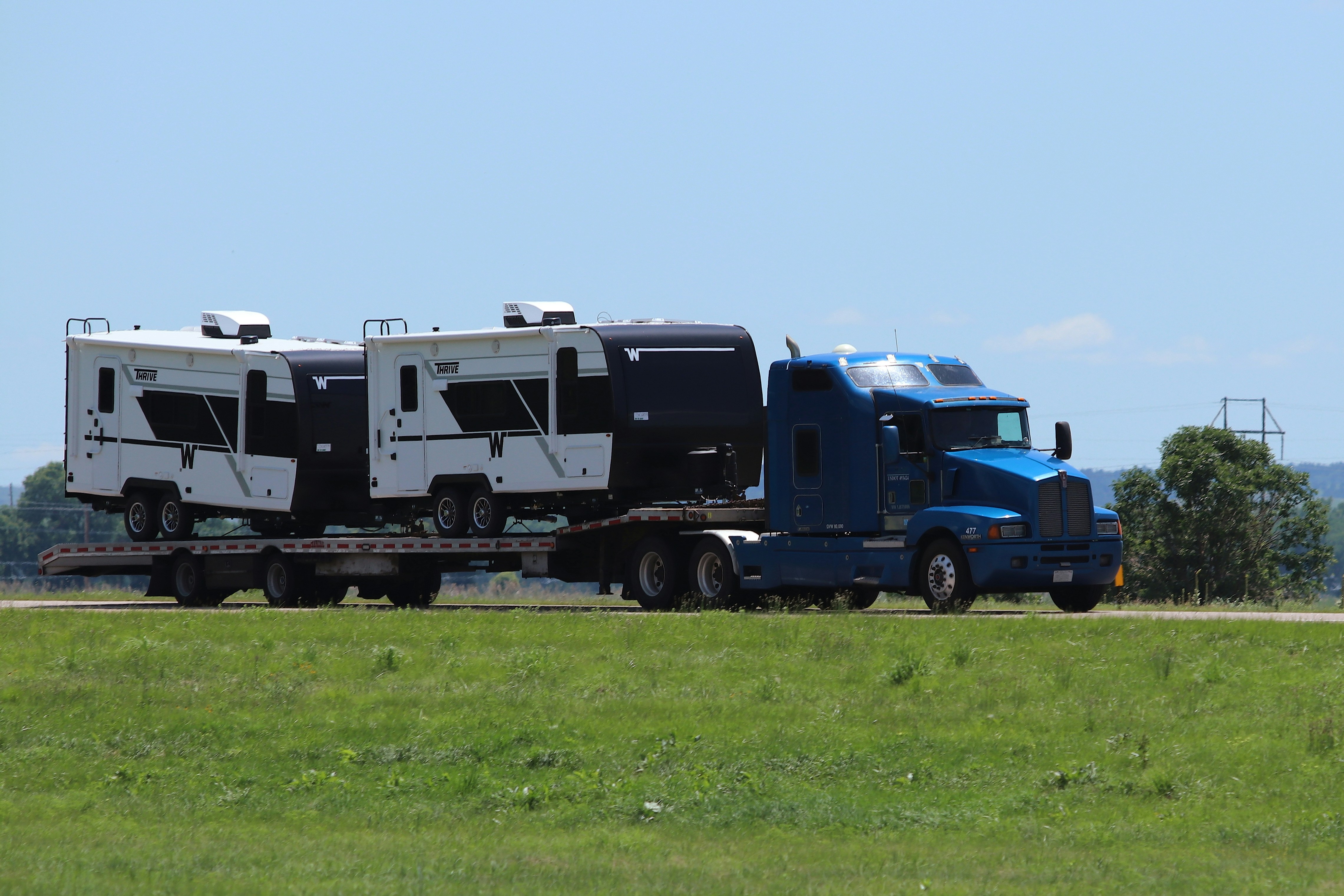Blue semi-truck hauling two campers on a flatbed trailer.