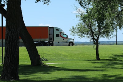 White semi-truck with orange trailer drives on road.
