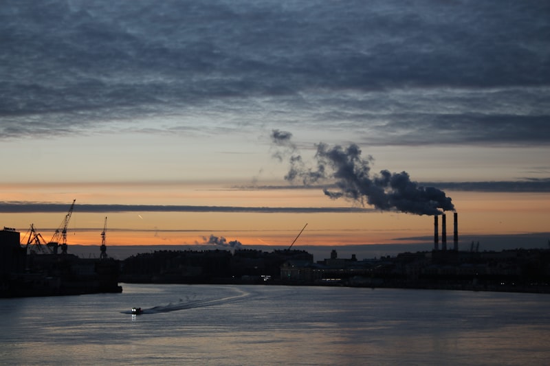 Industrial smokestacks emitting smoke at sunset over water