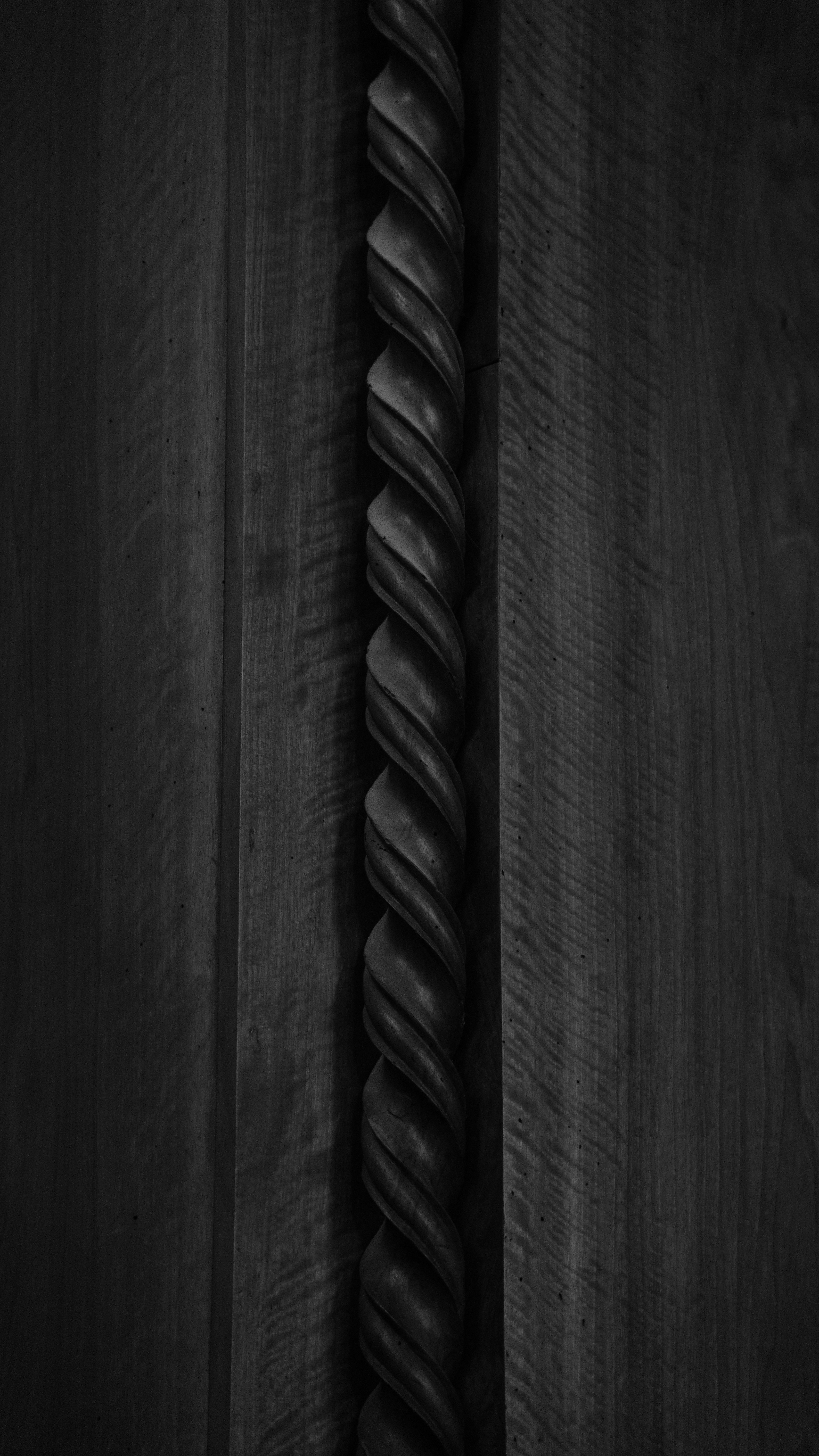 A dark, twisted wooden column against a wood grain background. photo ...