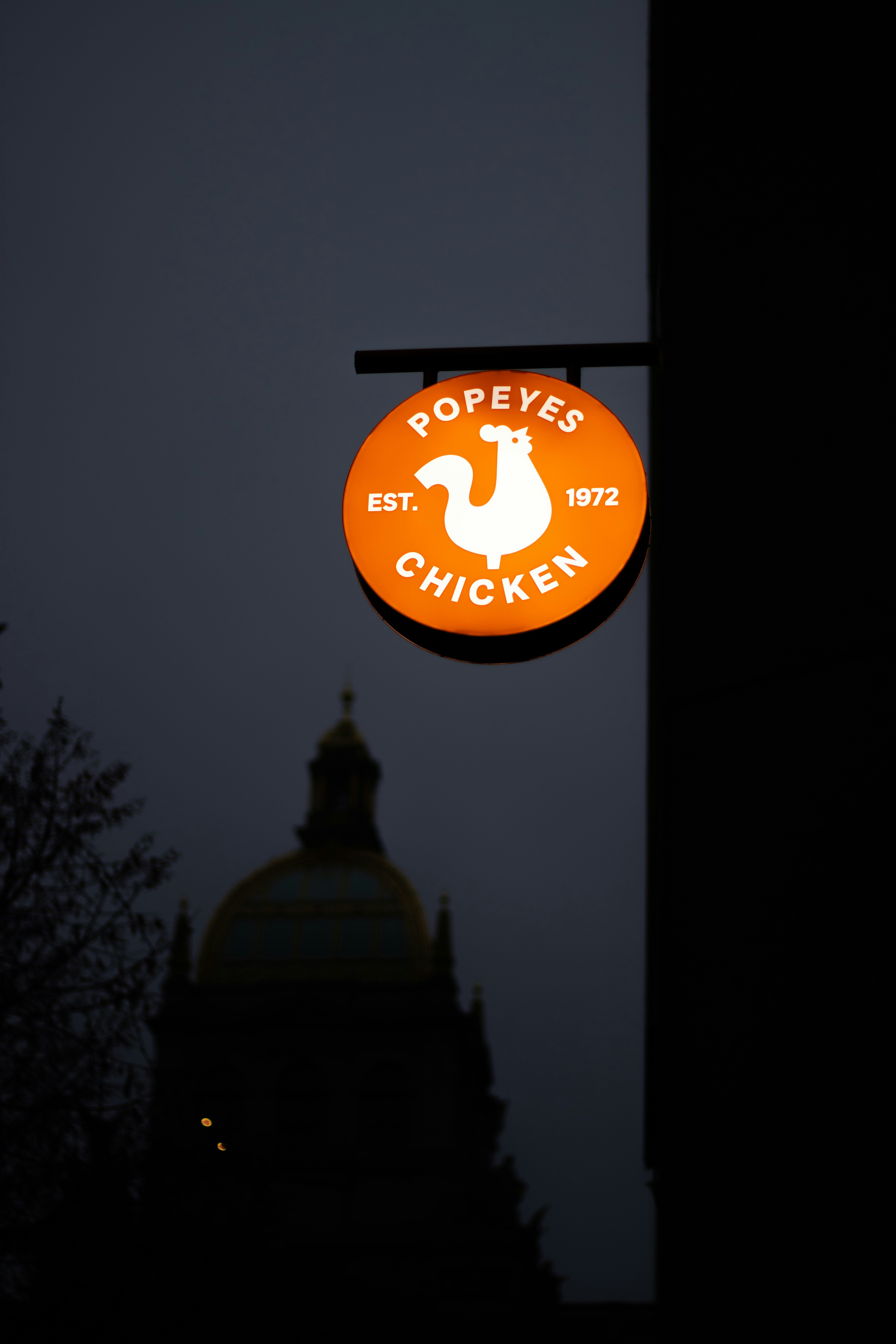 Popeyes chicken sign at dusk with building silhouette