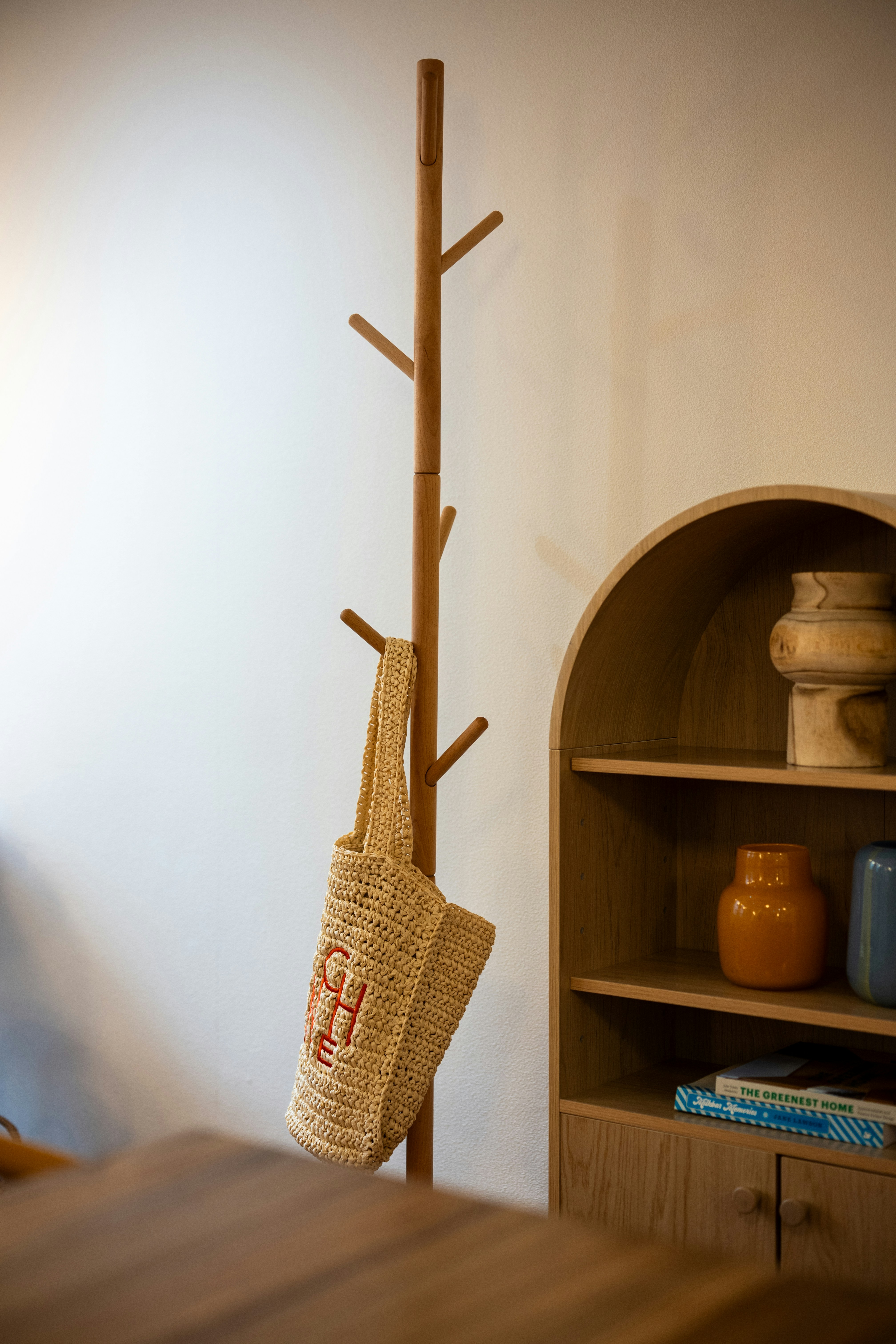 Straw tote bag hanging on a wooden coat rack.