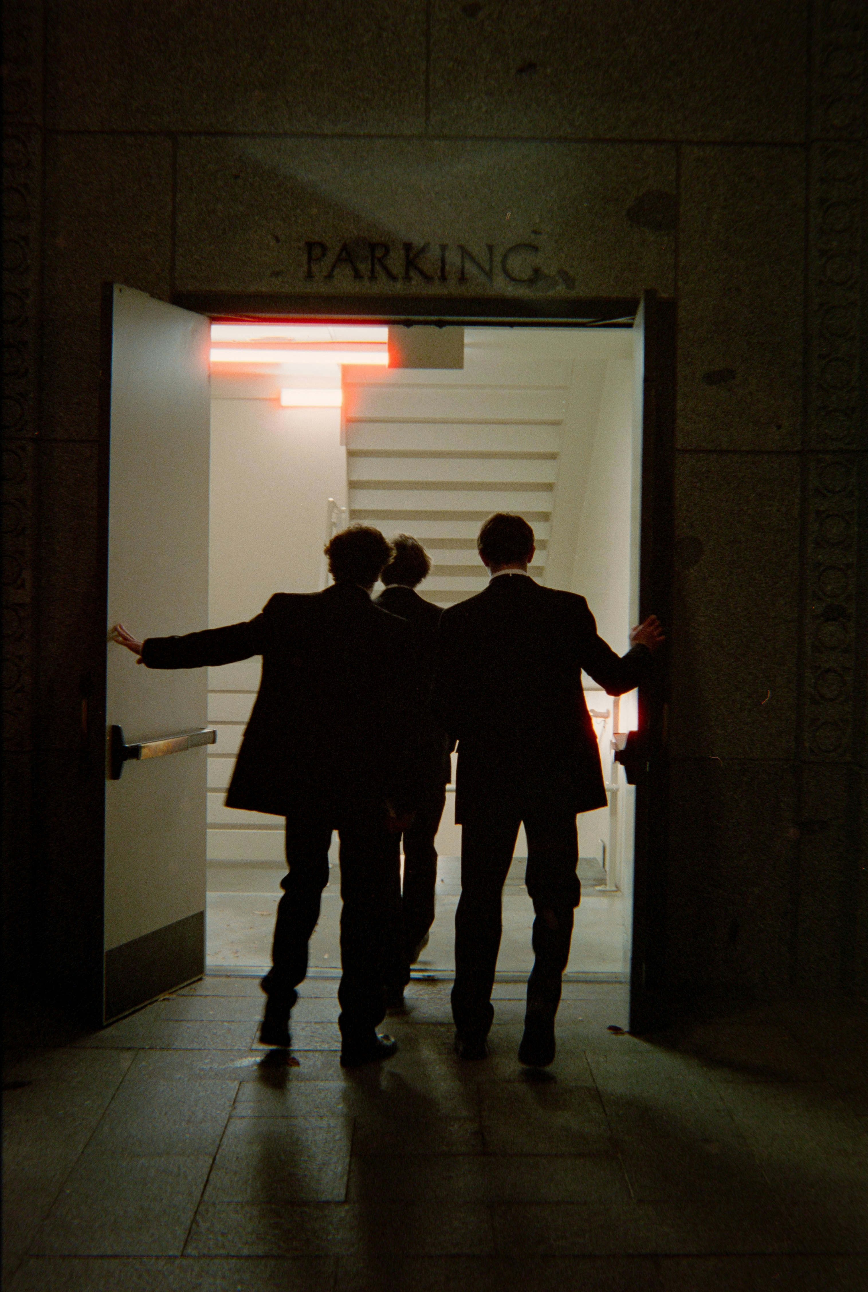 Three men in suits enter a parking garage.