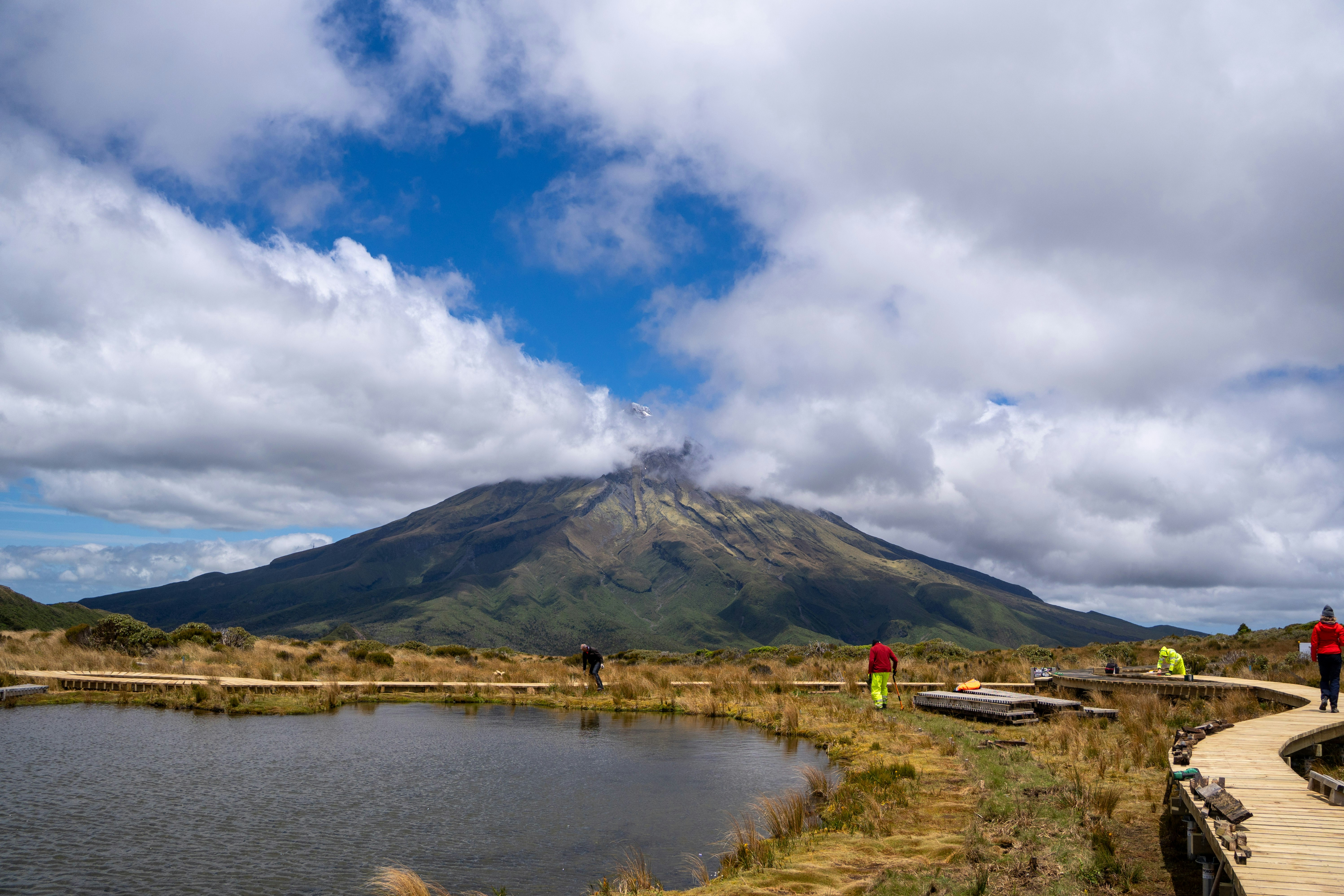 Hikers walk on a boardwalk near a mountain lake.