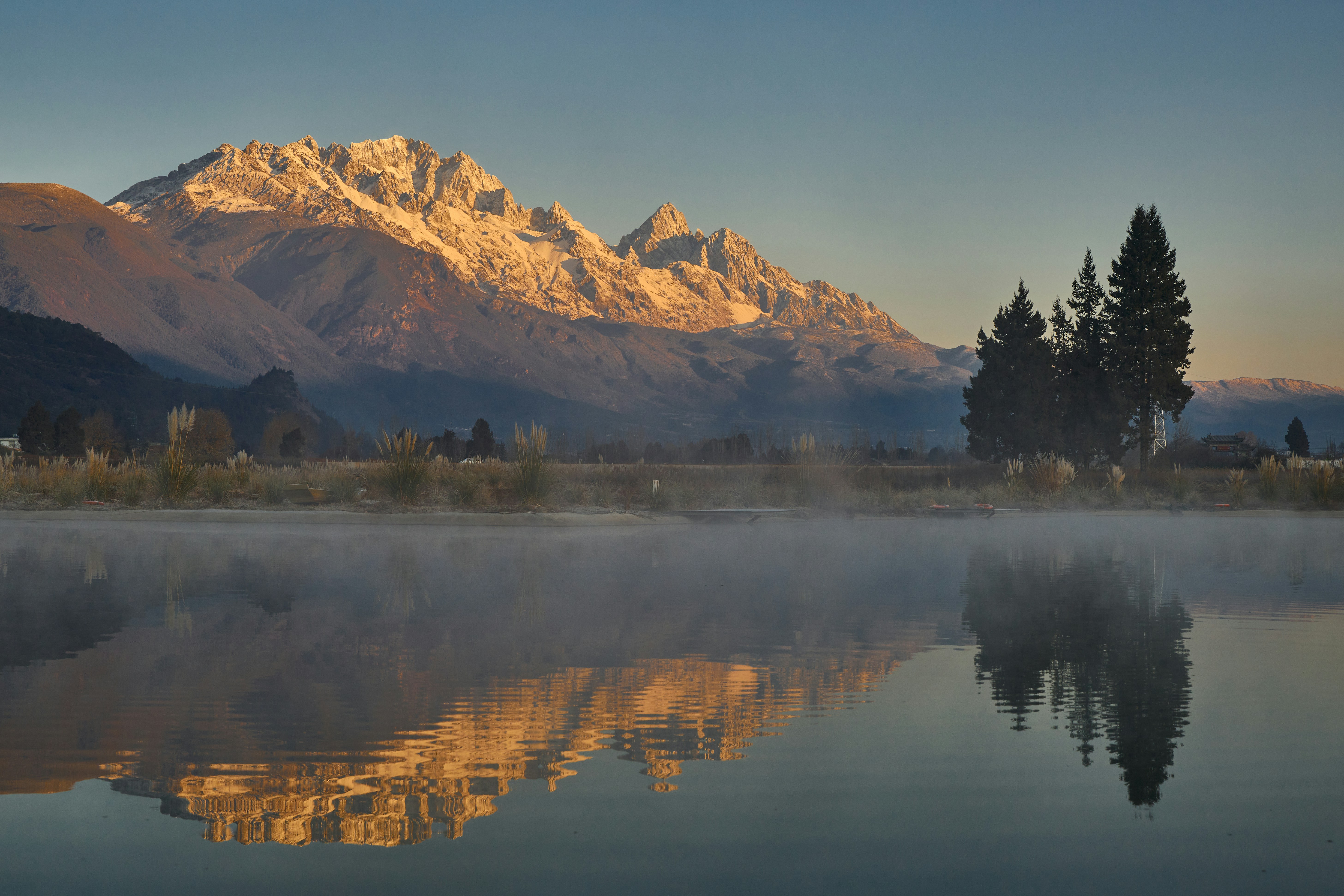 Le montagne innevate si riflettono in un lago tranquillo all'alba.