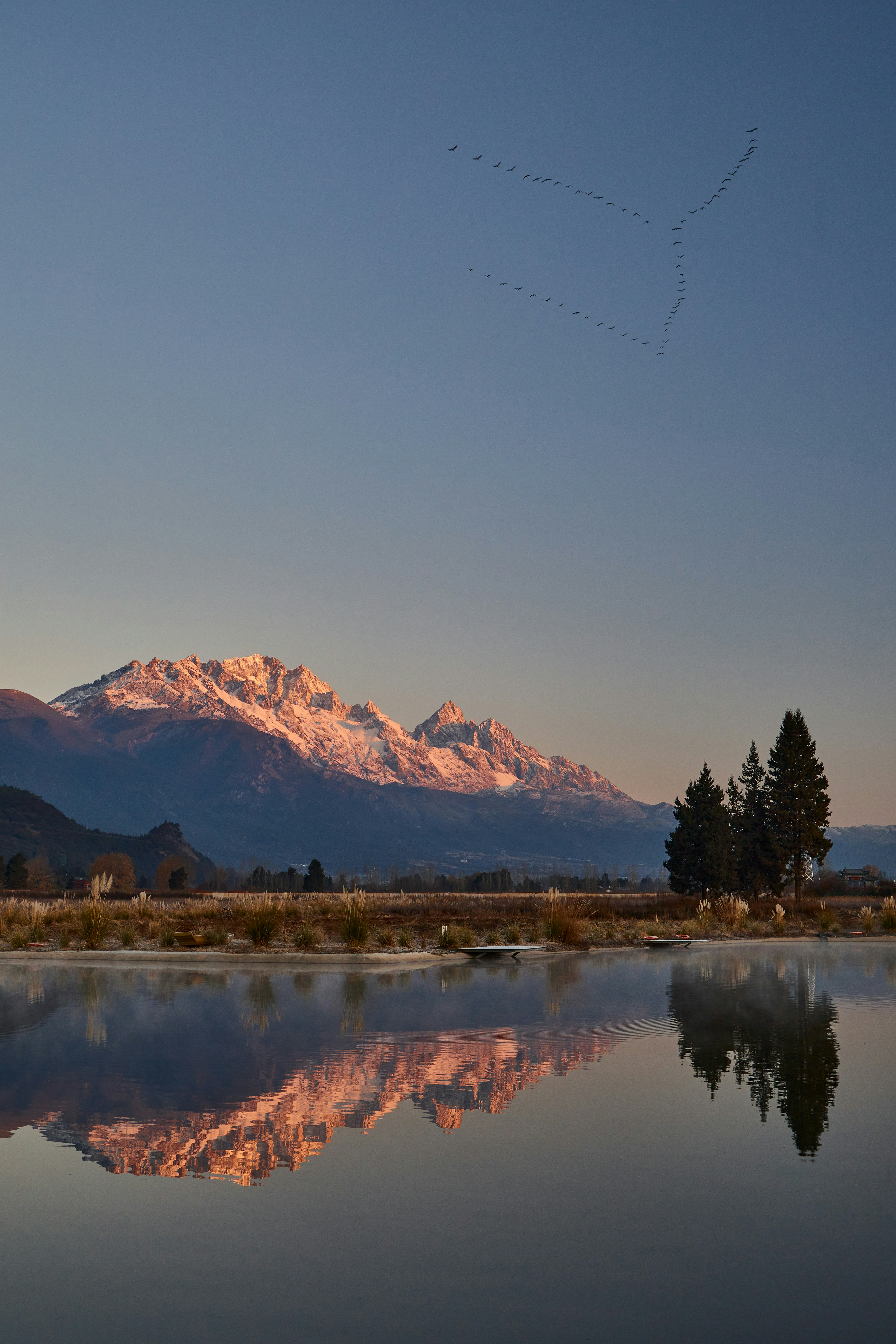 Montagne innevate riflesse nell'acqua calma all'alba.
