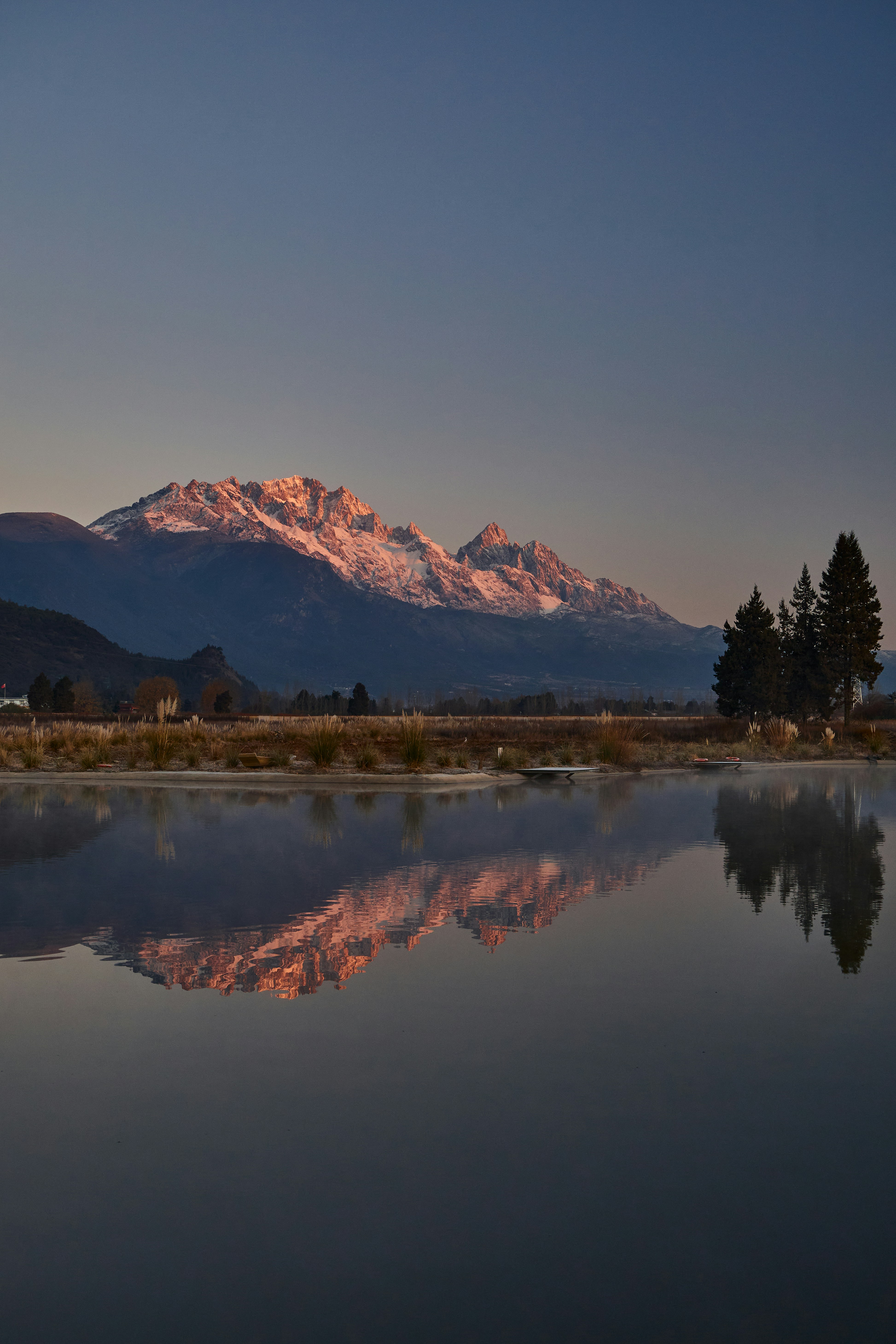 Le montagne innevate si riflettono nell'acqua calma all'alba.