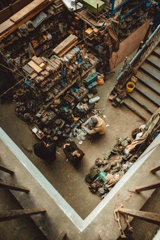 Two people working in a cluttered workshop with spare parts.