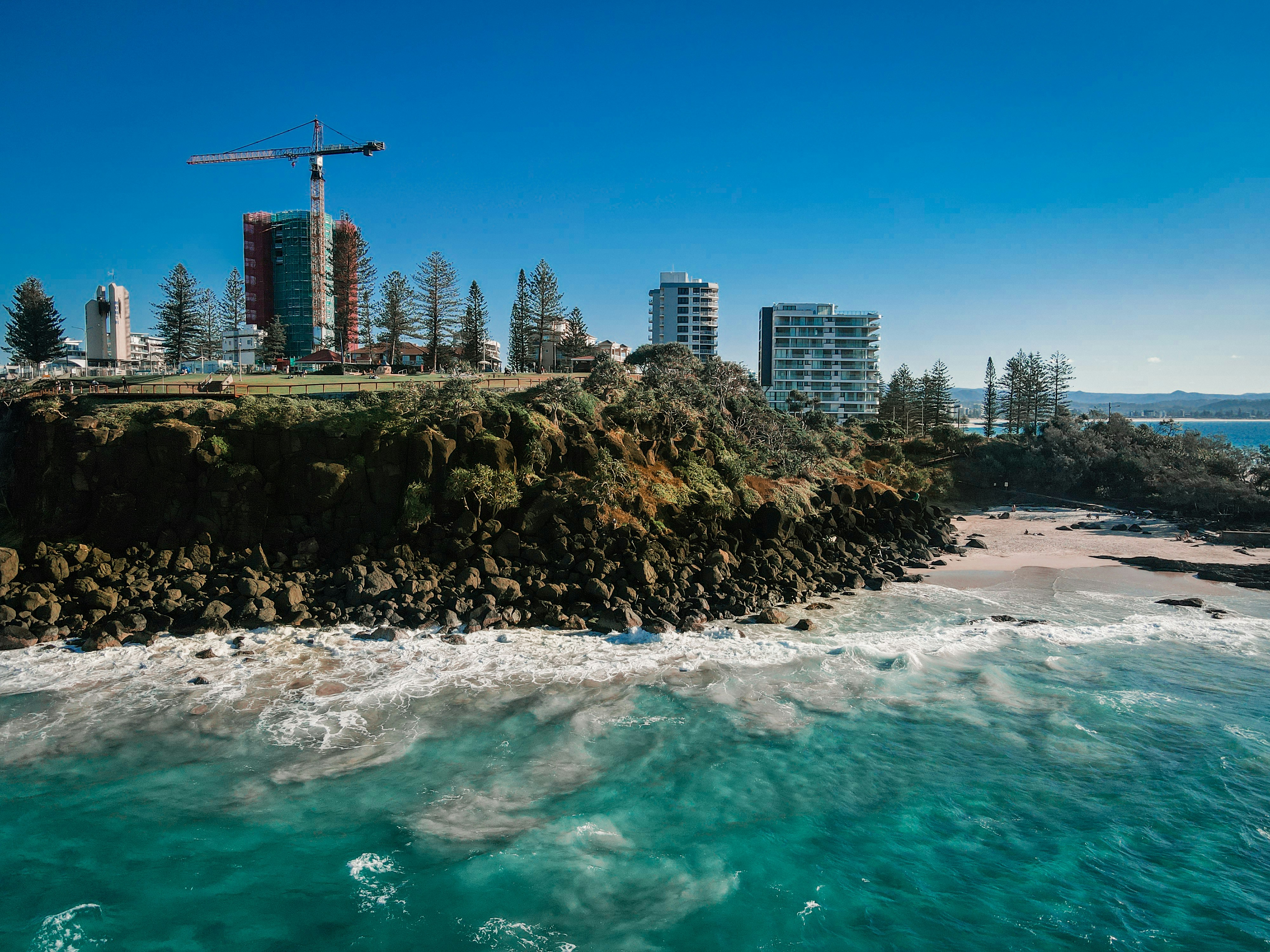 Coastal city skyline with ocean waves and rocky shore.