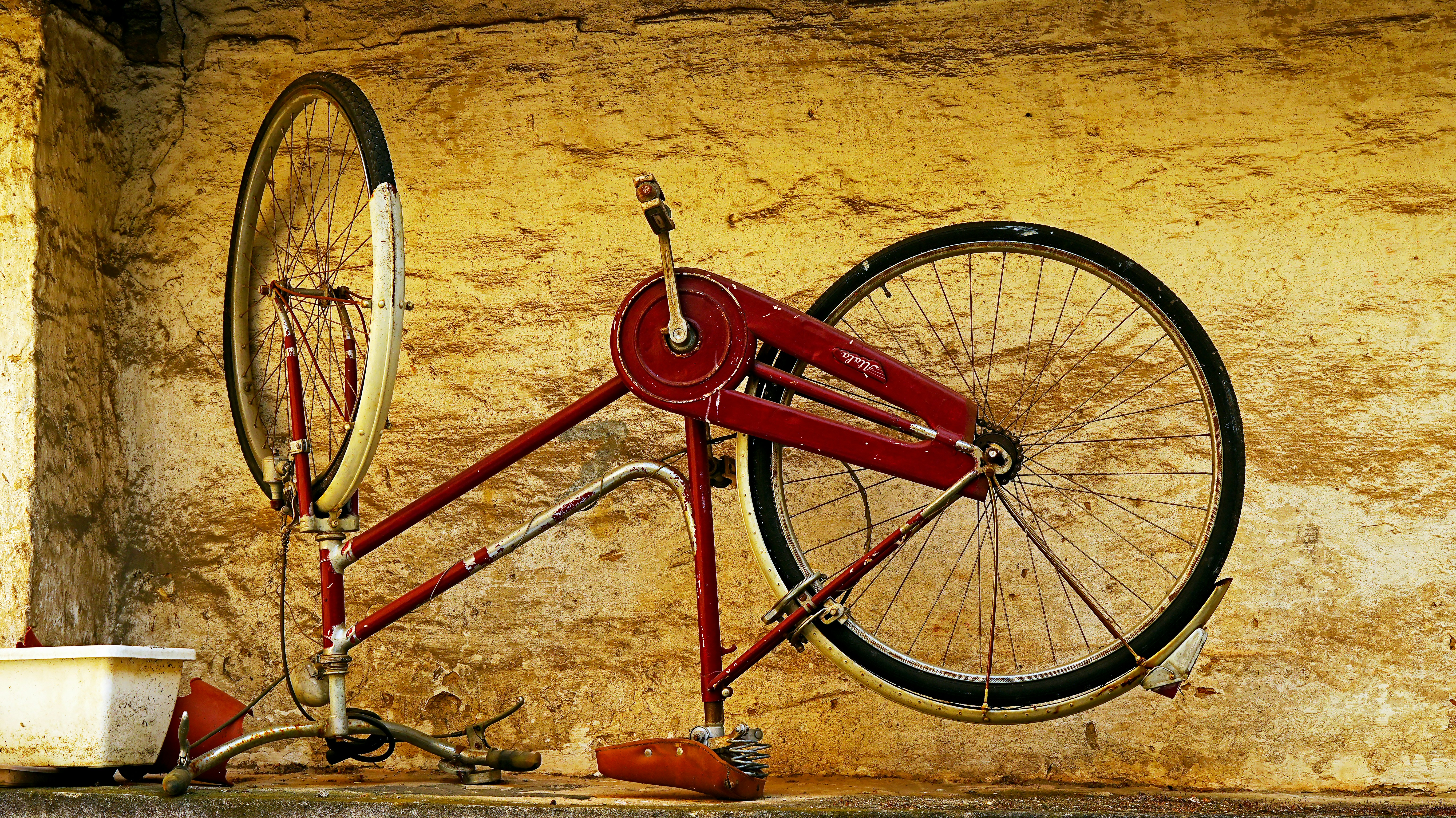 A vintage red bicycle frame against a textured wall.