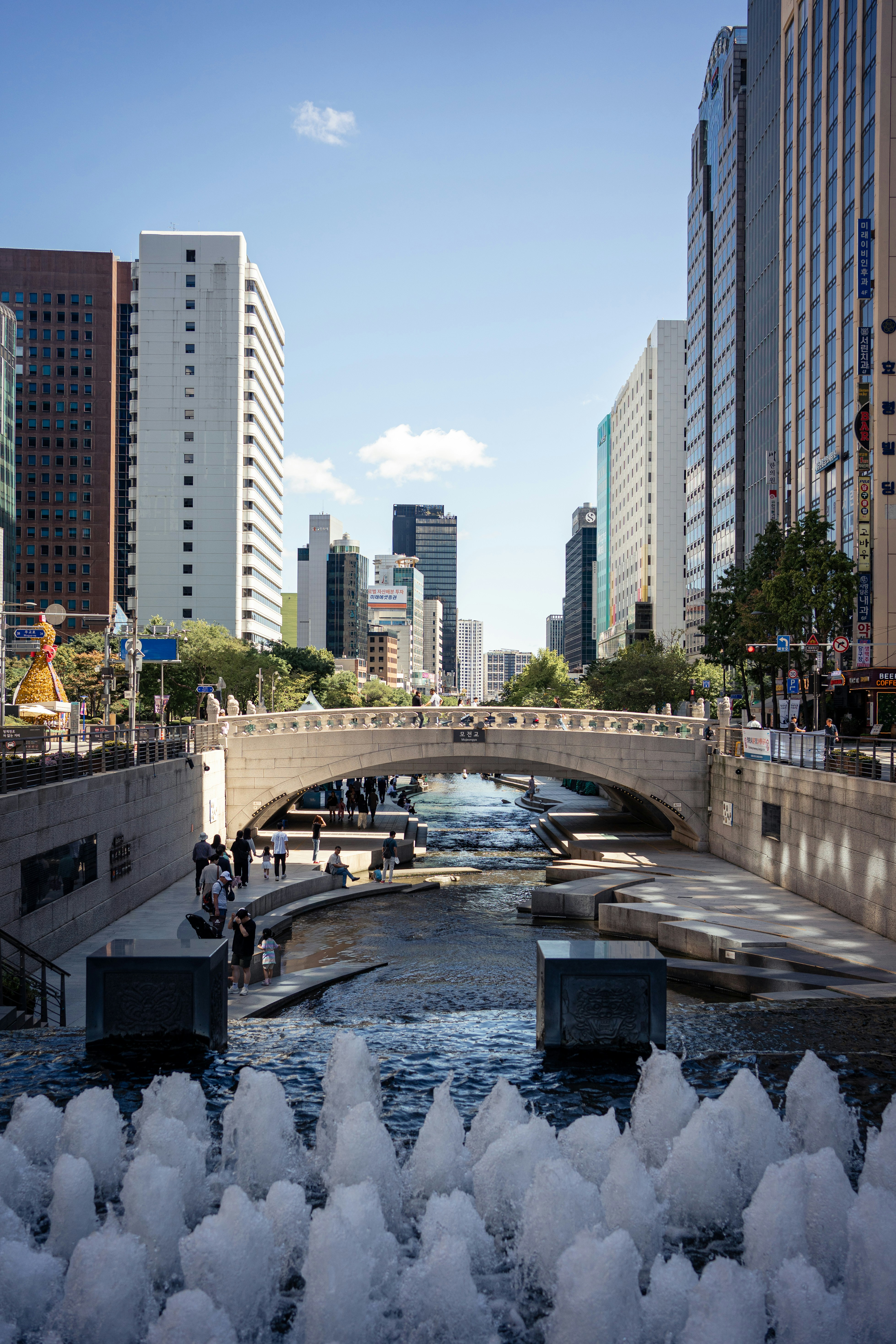Modern city buildings flank a canal with a bridge.