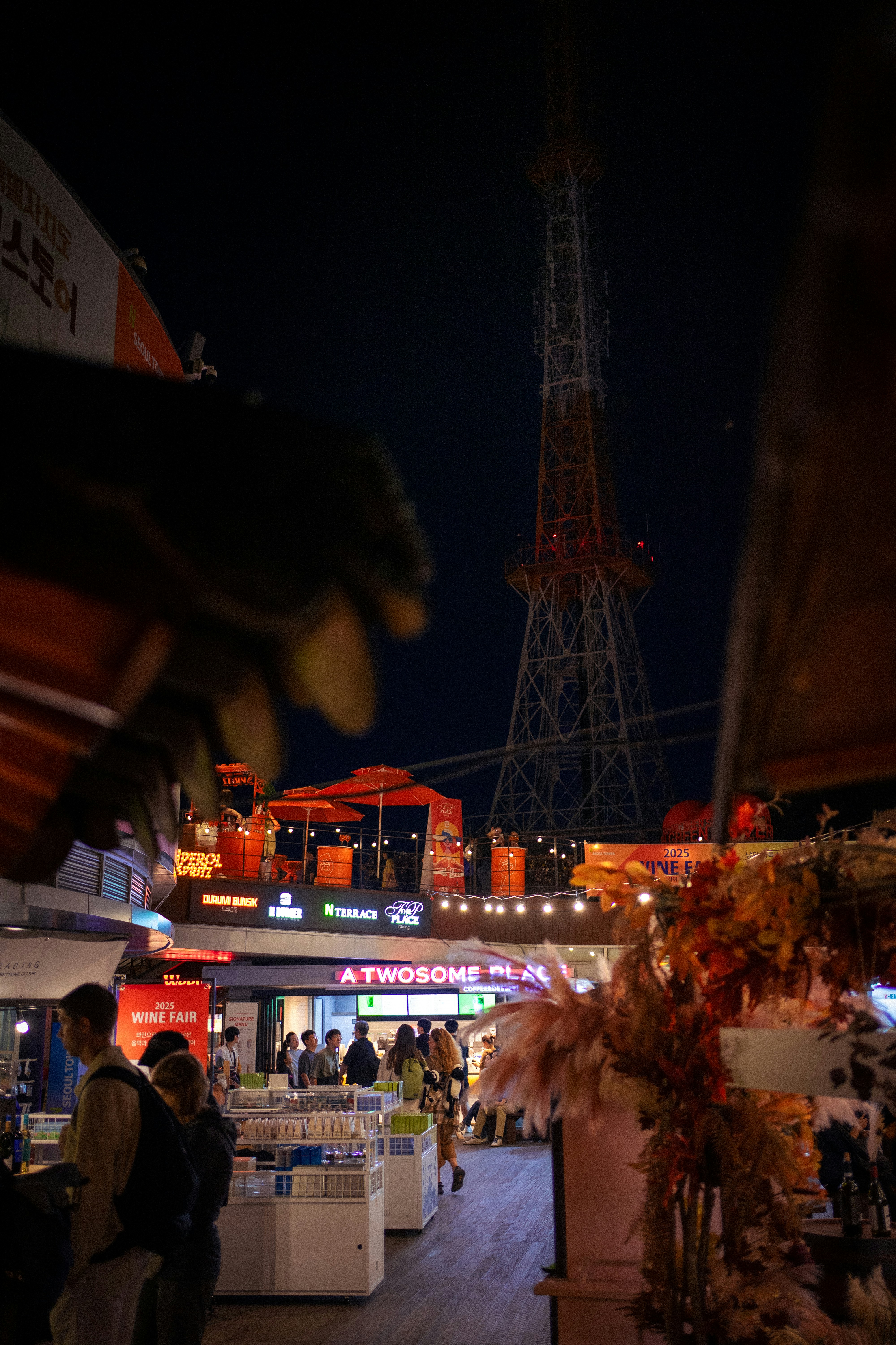 City street at night with tall tower and shops.