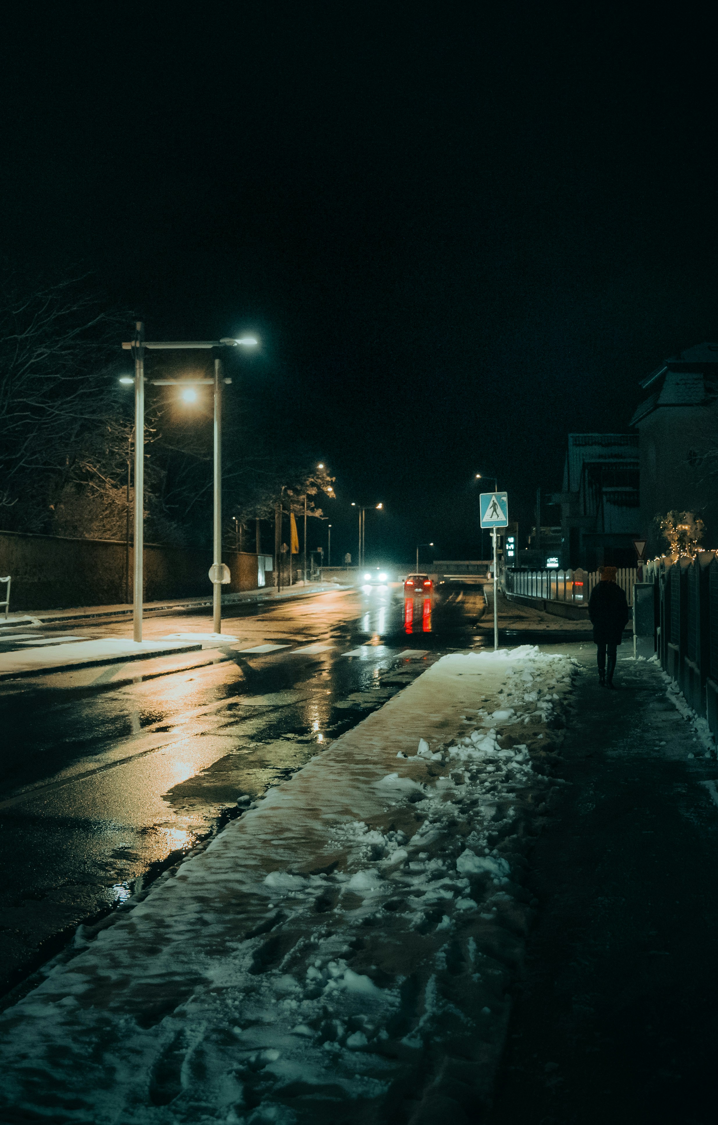 A person walks down a snowy city street at night.