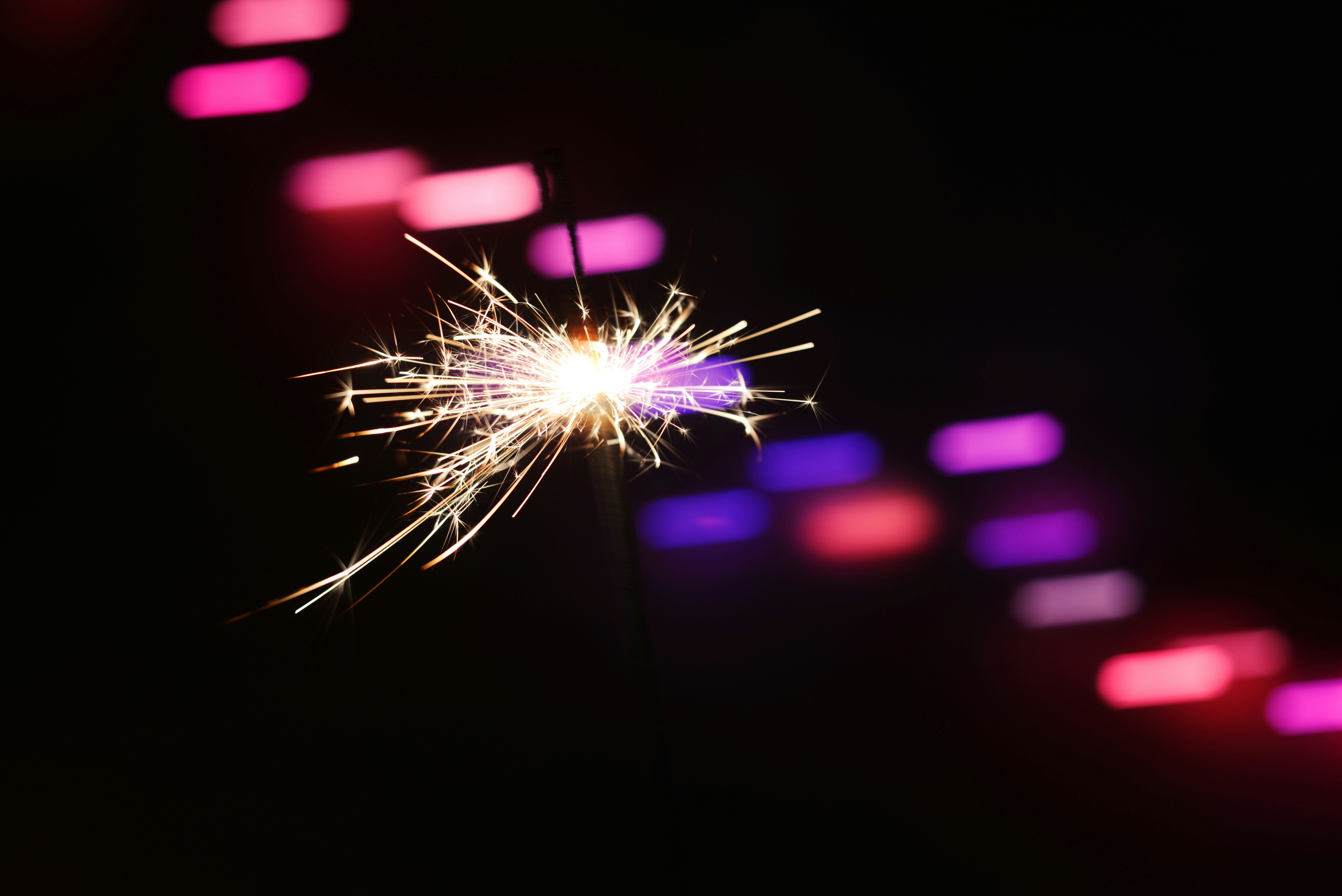 Sparkler ignites with colorful bokeh lights in background