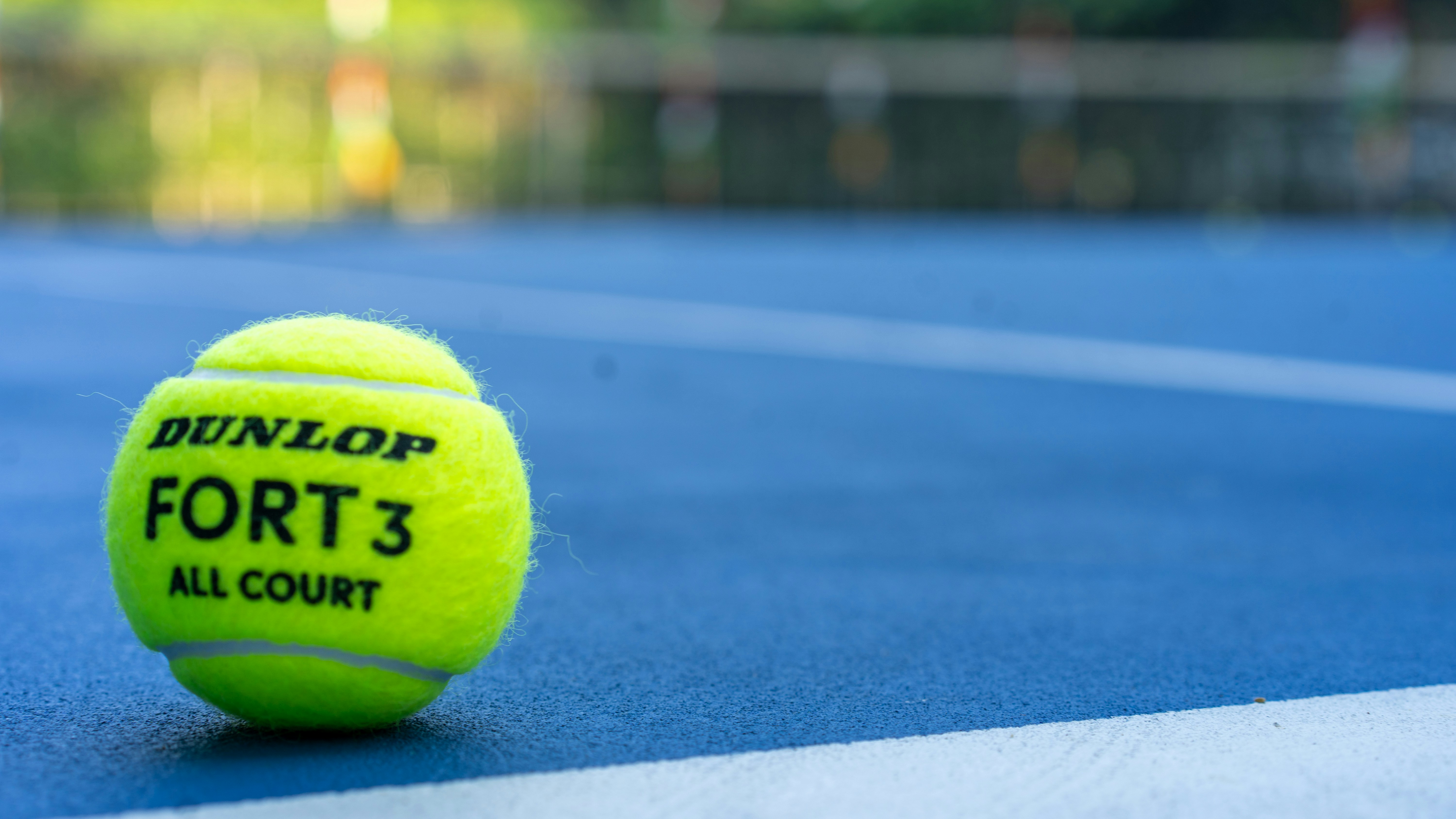 A neon yellow tennis ball rests on a blue court.