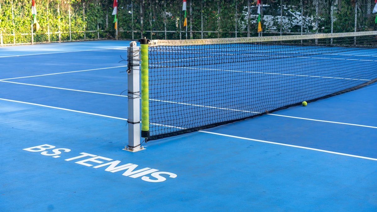 Blue tennis court with net and ball on a sunny day