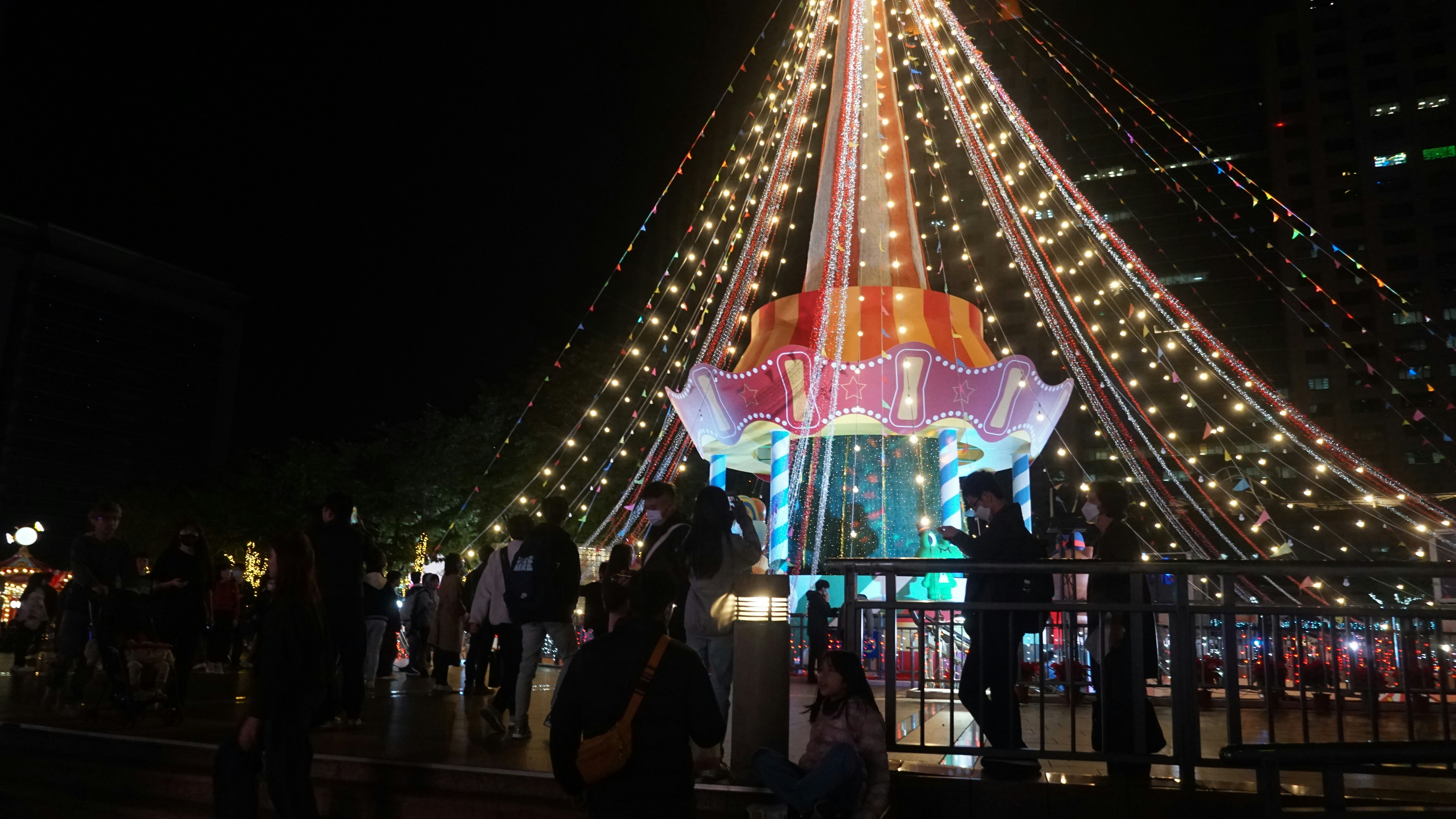 People gather around a brightly lit amusement ride at night.