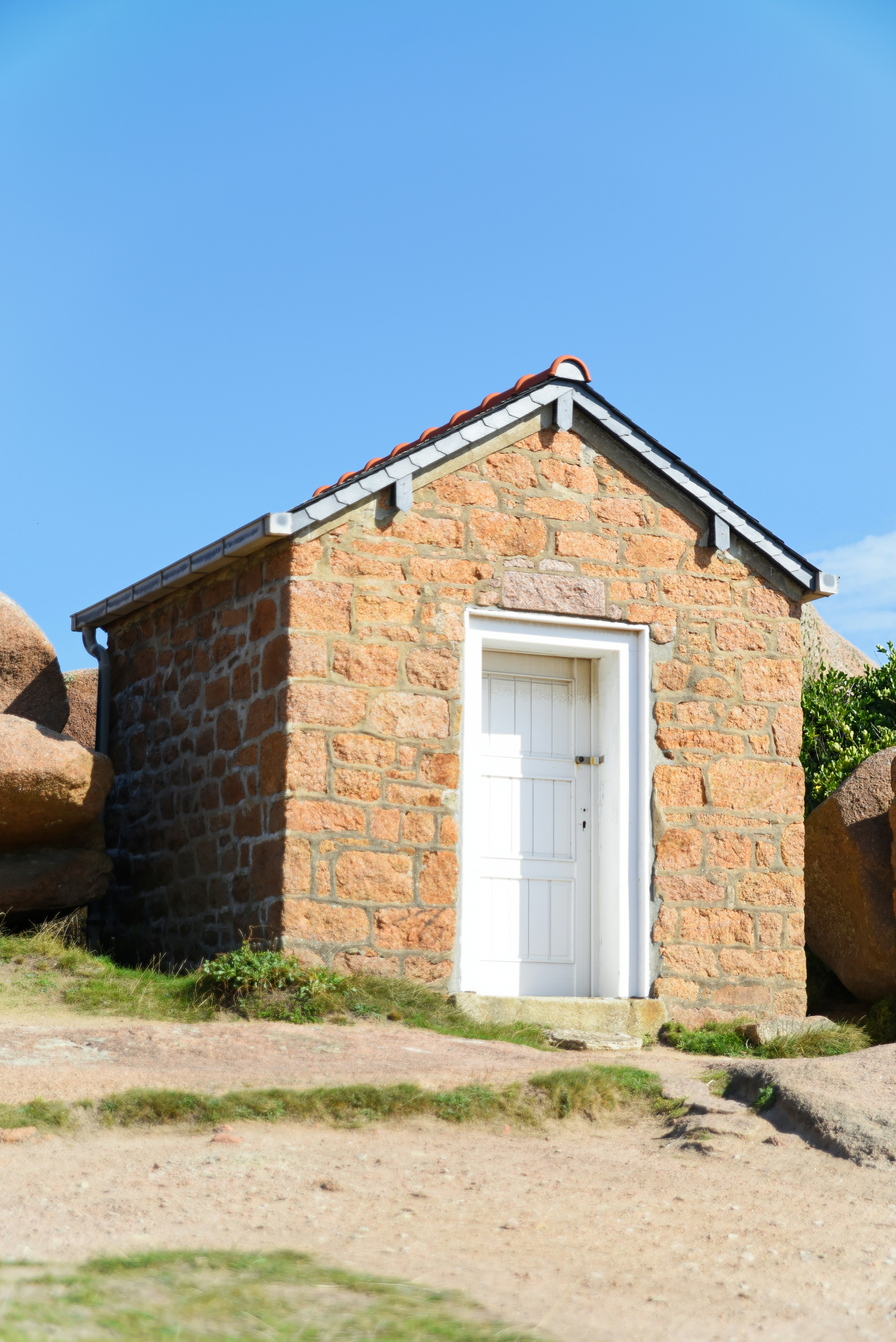 Small stone building with a white door under blue sky.